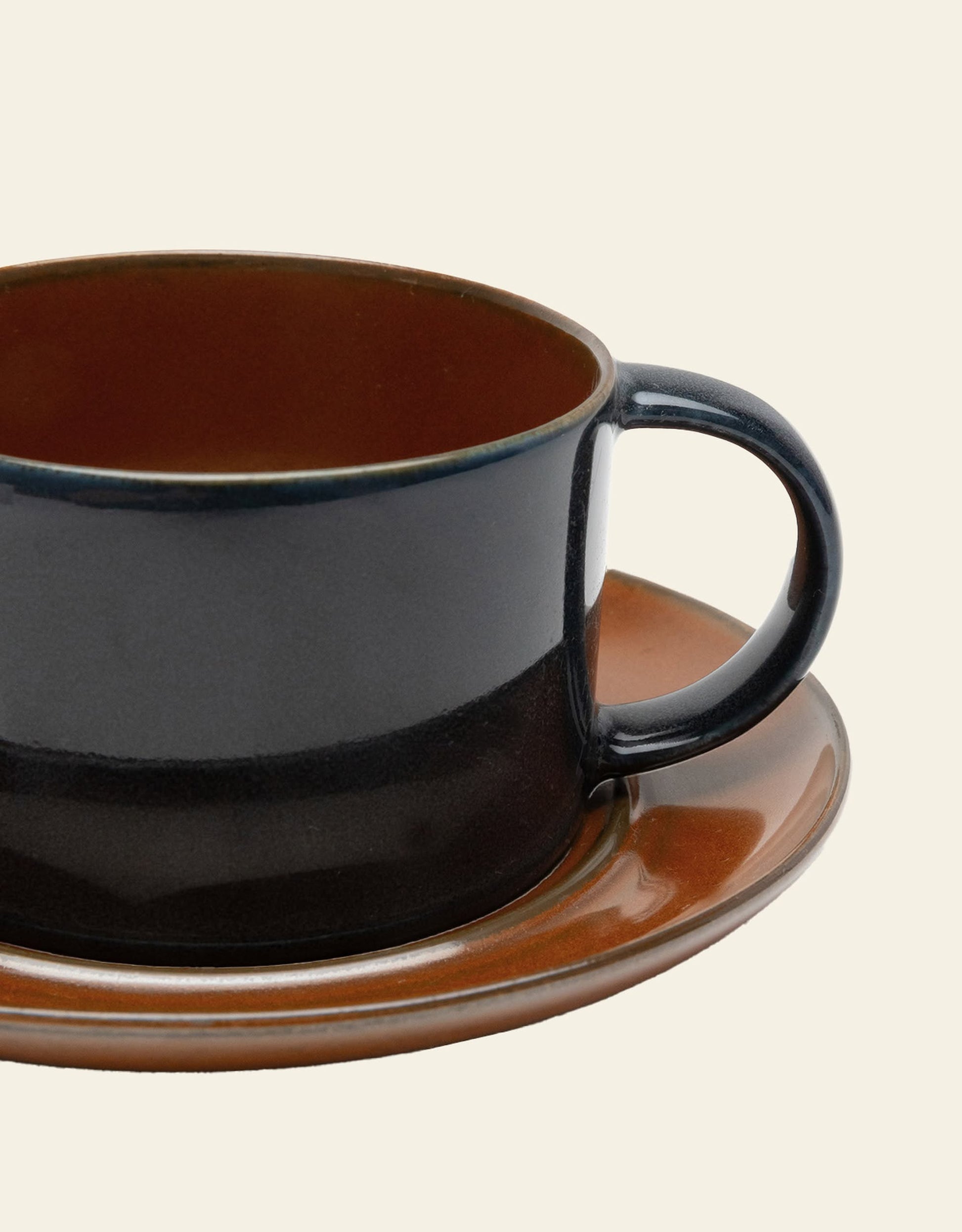 A close-up of the Serax Terres De Rêves Coffee Cup by Serax, a dark brown stoneware cup with handle on a matching saucer, set against a plain light background.