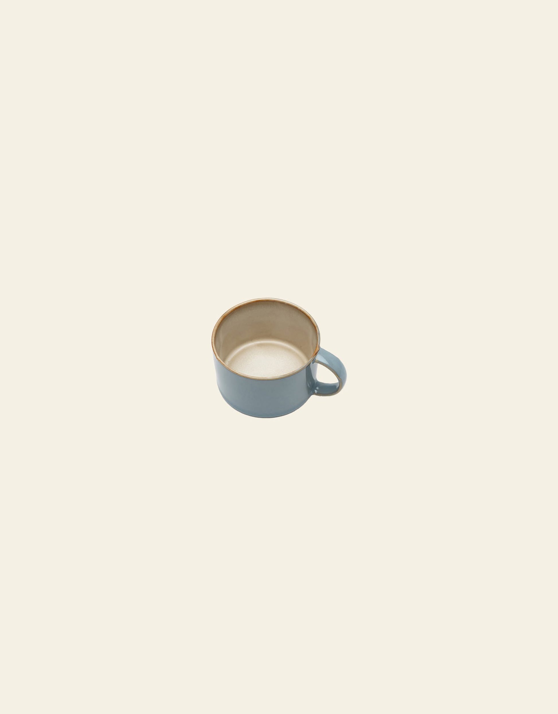 The Serax Terres De Rêves Coffee Cup by Serax is a handcrafted blue stoneware cup with a handle, shown from above and at an angle against a plain, light beige background.