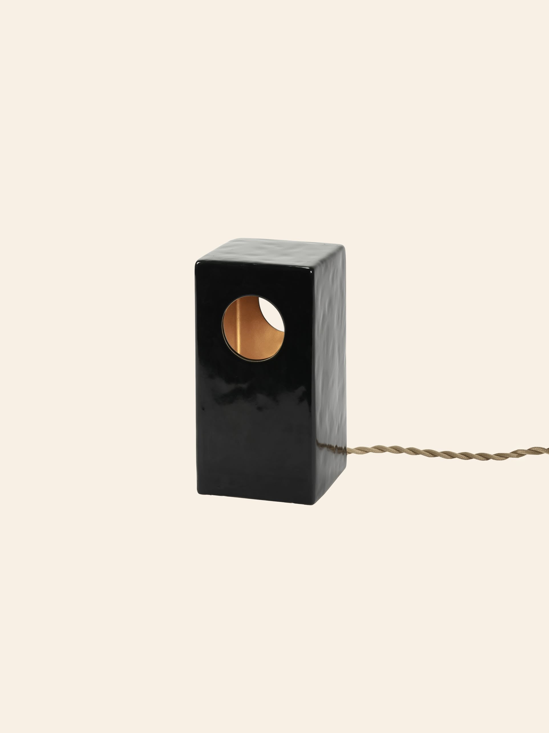 The Serax Terres De Rêves Maxime N°1 Table Lamp in glossy black stoneware features a rectangular geometric design with a gold-accented circular cutout, braided power cord, and brand signature style.