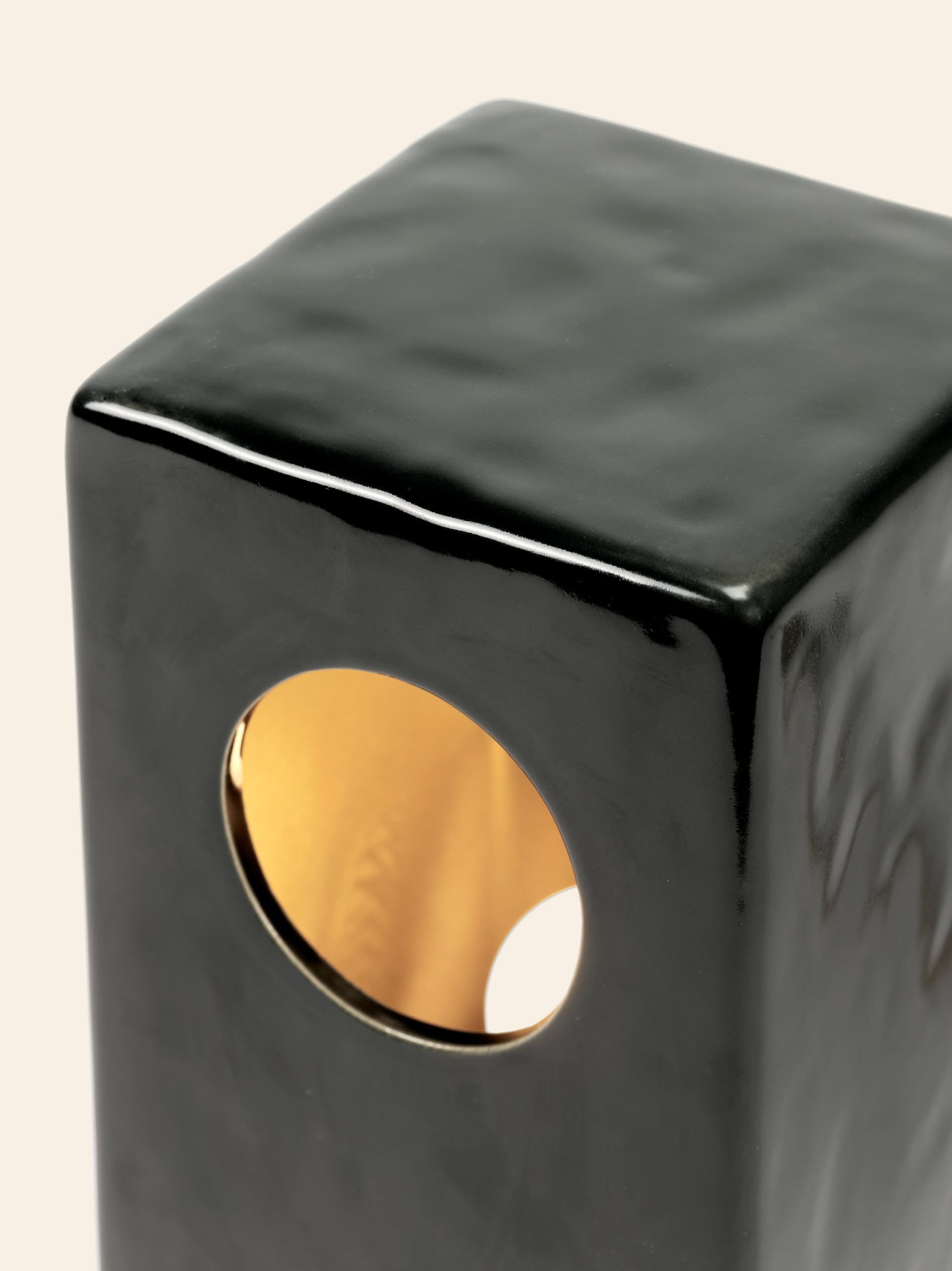 Close-up of the Serax Terres De Rêves Maxime N°1 Table Lamp by Serax in glossy black, featuring a rectangular shape with rounded edges and a circular gold-accented opening, highlighting its geometric design against a light beige background.