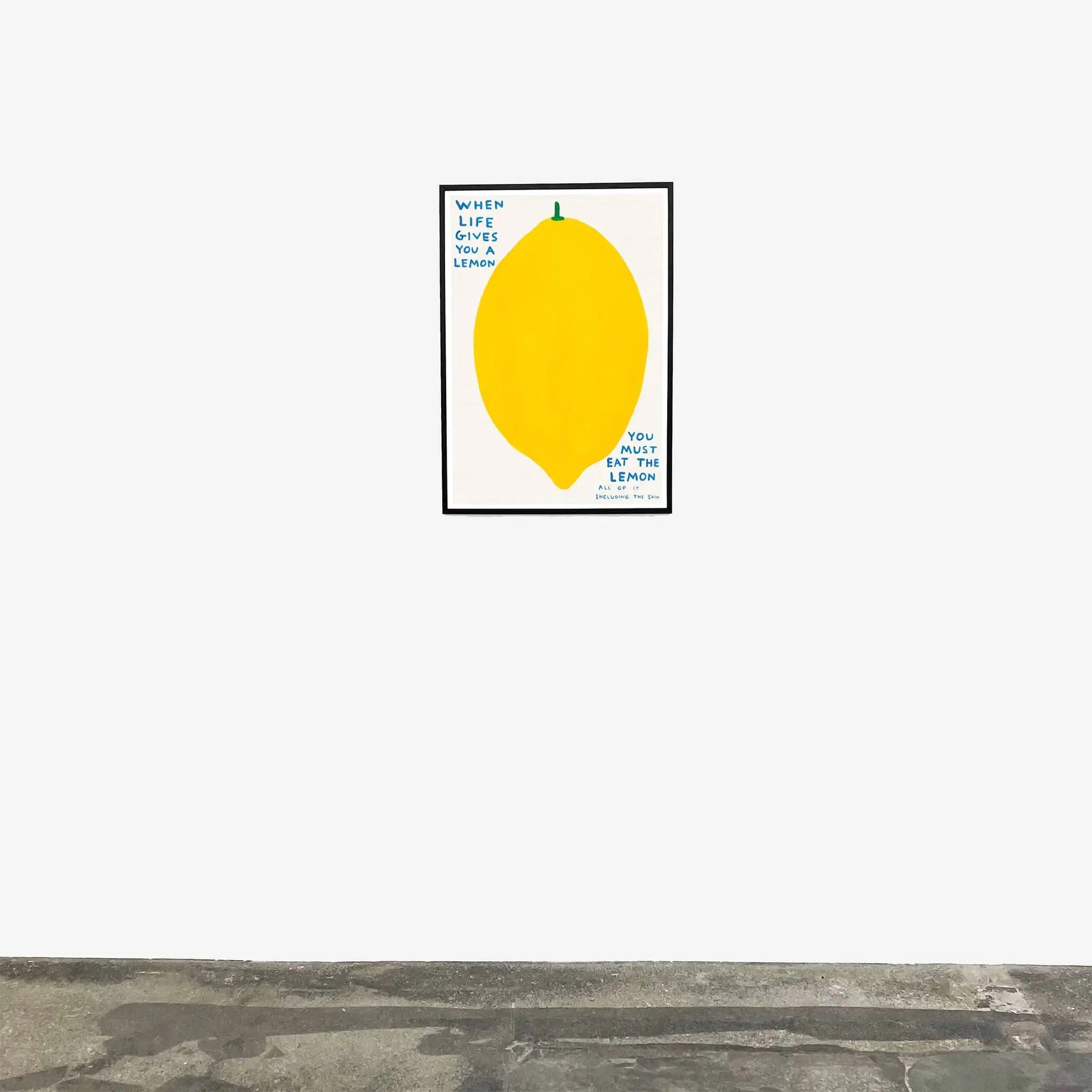A framed Shrig Shop David Shrigley - When Life Gives You A Lemon (60x80) poster featuring a large yellow lemon and quirky text hangs above a stone floor—a unique wall art piece by Shrig Shop.