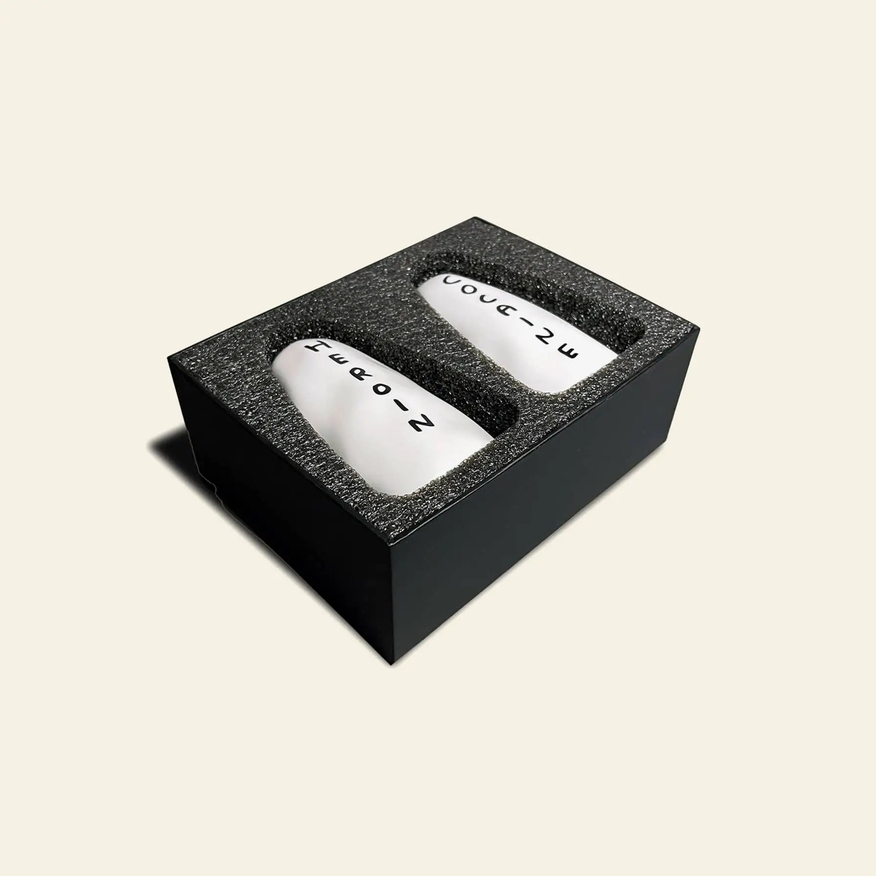 The Shrig Shop Heroin and Cocaine Porcelain Shakers by Shrig Shop are two white, oval shakers labeled with black text and numbers, housed in a black foam-padded box—a collectible set inspired by David Shrigley.