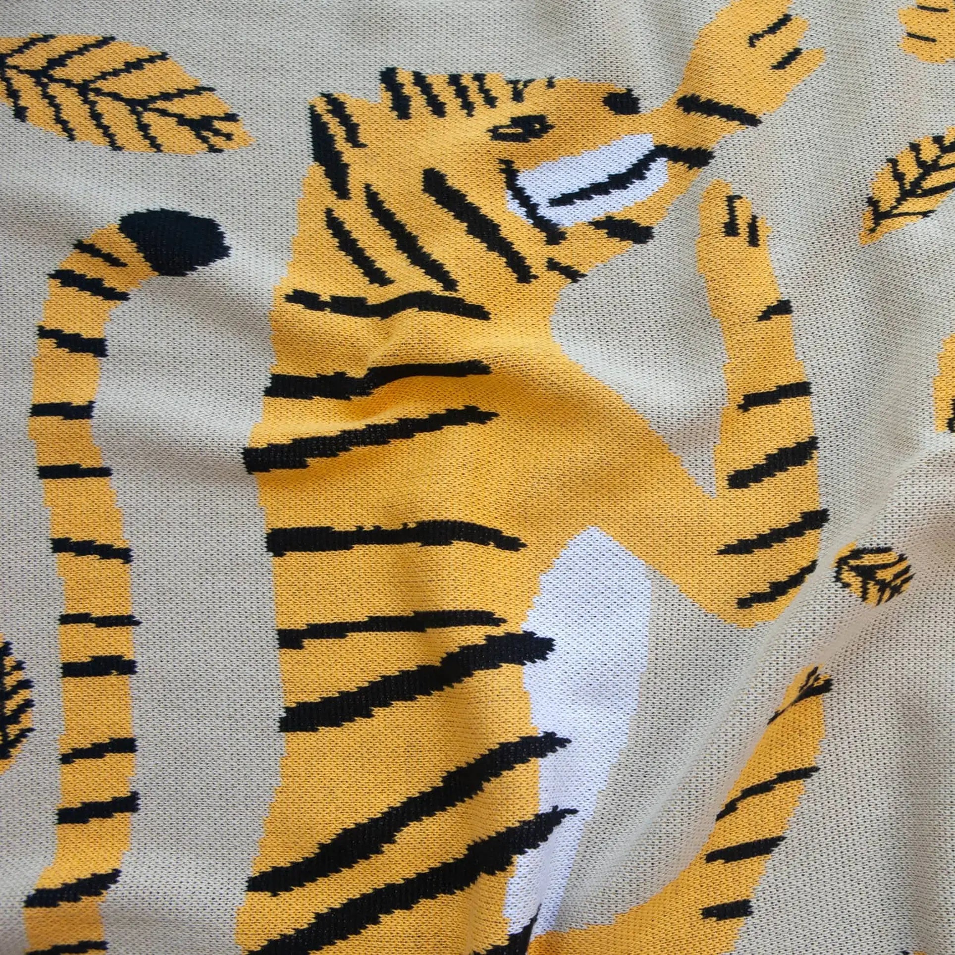 A recycled cotton blend fabric featuring playful yellow, black, and white tigers with stylized leaves, inspired by the Slowdown Studio Big Cats Mini Blanket.
