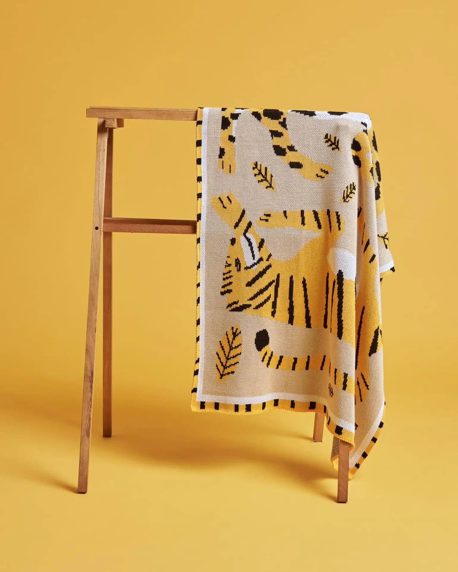 The Slowdown Studio Big Cats Mini Blanket features a playful tiger and leaf pattern in yellow and white recycled cotton blend, set on a yellow background.