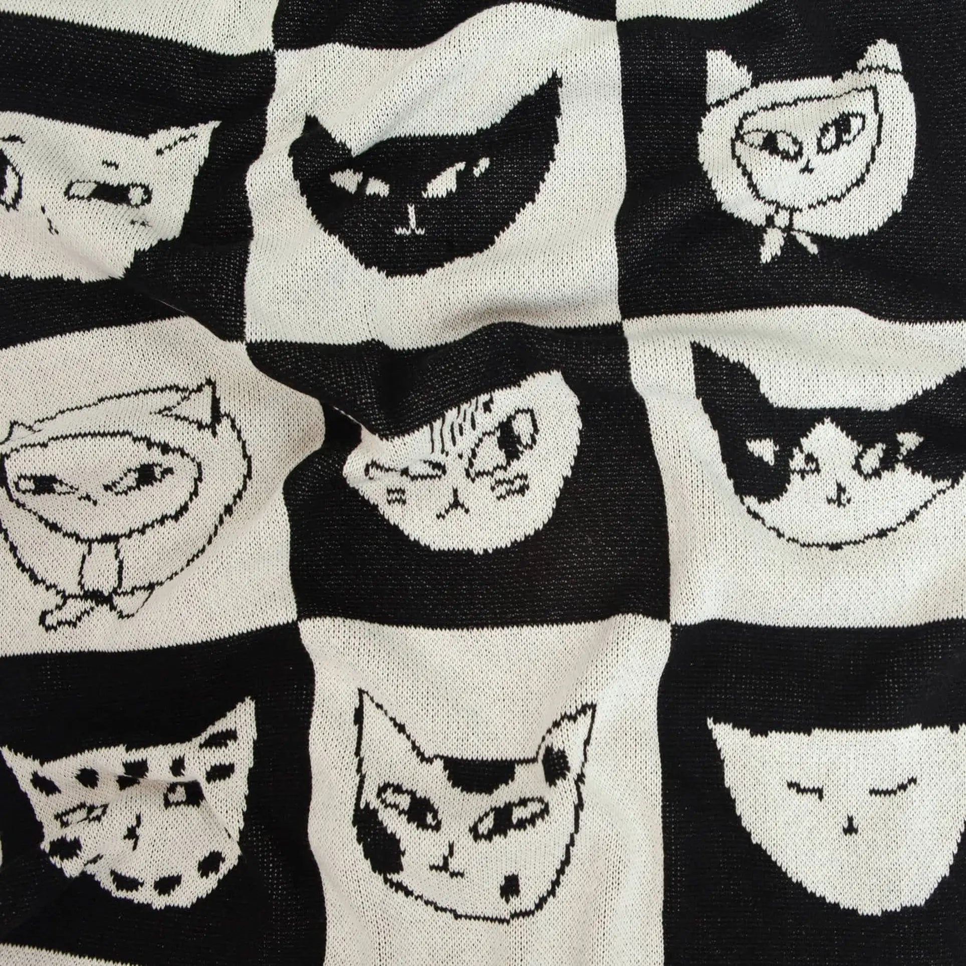 The Slowdown Studio Cat Bingo Mini Blanket features a black and white grid of cartoon cat faces with different expressions, crafted from a soft recycled cotton blend by Slowdown Studio.