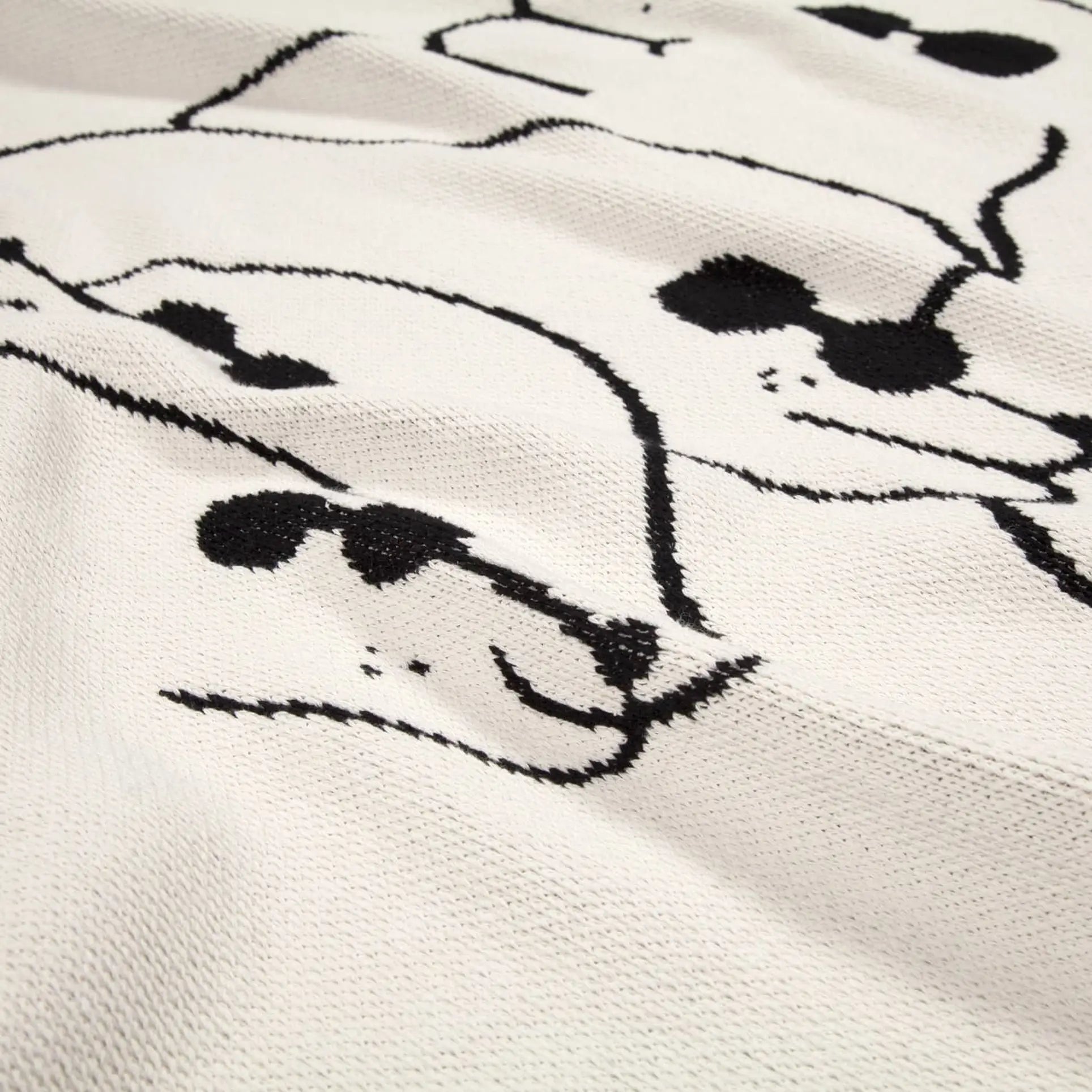 The Slowdown Studio Dawgs Mini Blanket features a playful white textured fabric with abstract dog faces in sunglasses, crafted from recycled cotton—perfect for adding style and fun to any space.