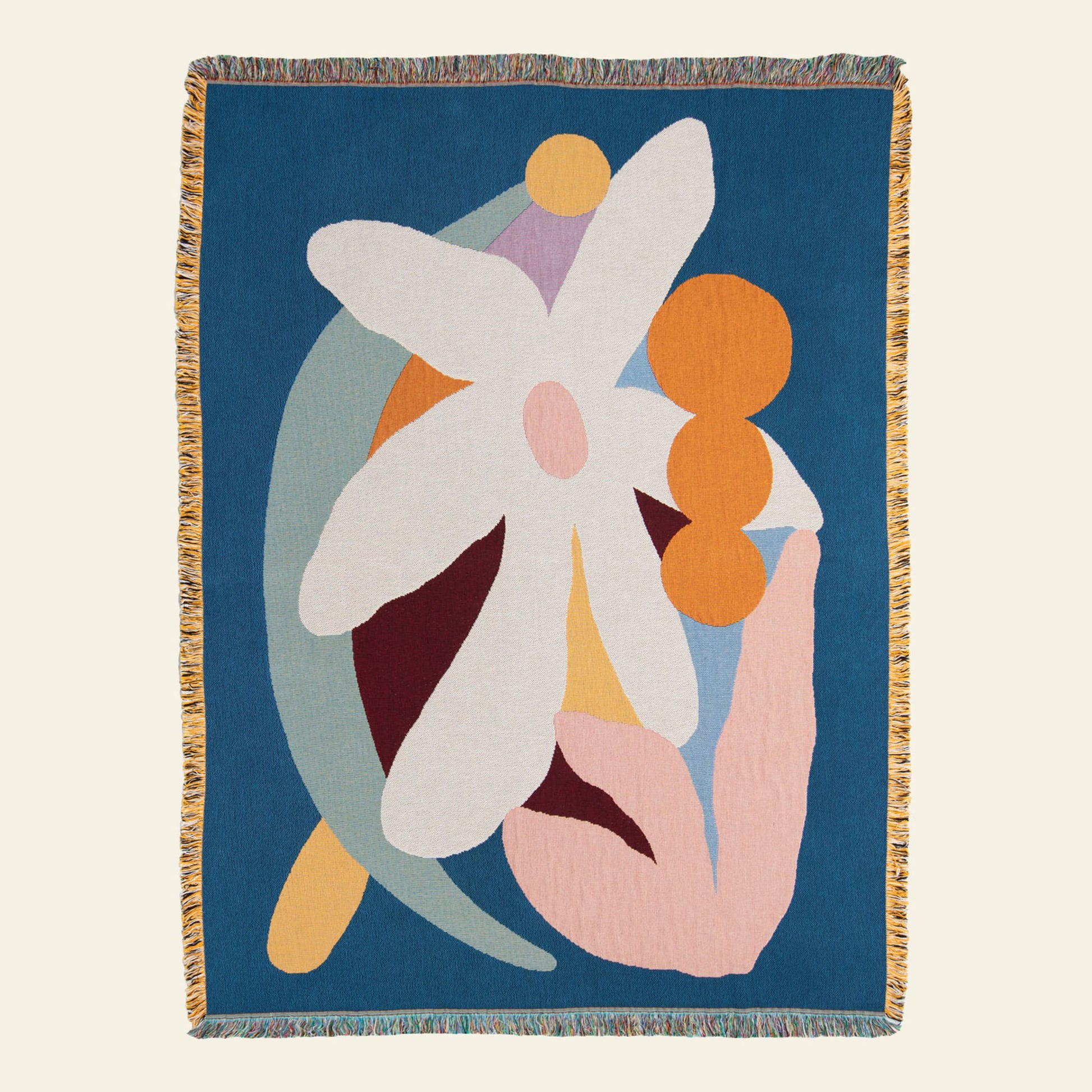 The Slowdown Studio Delaney Throw by Slowdown Studio is an eco-friendly woven blanket made from recycled cotton, featuring multicolored abstract shapes, a large white flower, orange circles, pastel accents, and vibrant fringed edges on deep blue.