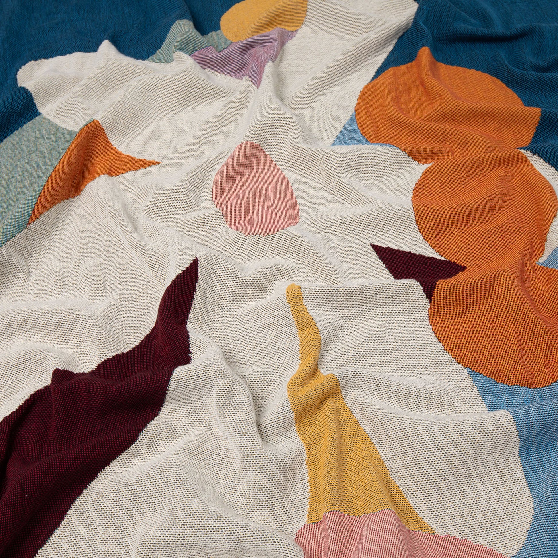 The Slowdown Studio Delaney Throw by Slowdown Studio features abstract, colorful shapes in orange, blue, yellow, maroon, pink, and white atop a soft eco-friendly fabric with an irregular overlapping pattern and gentle folds.