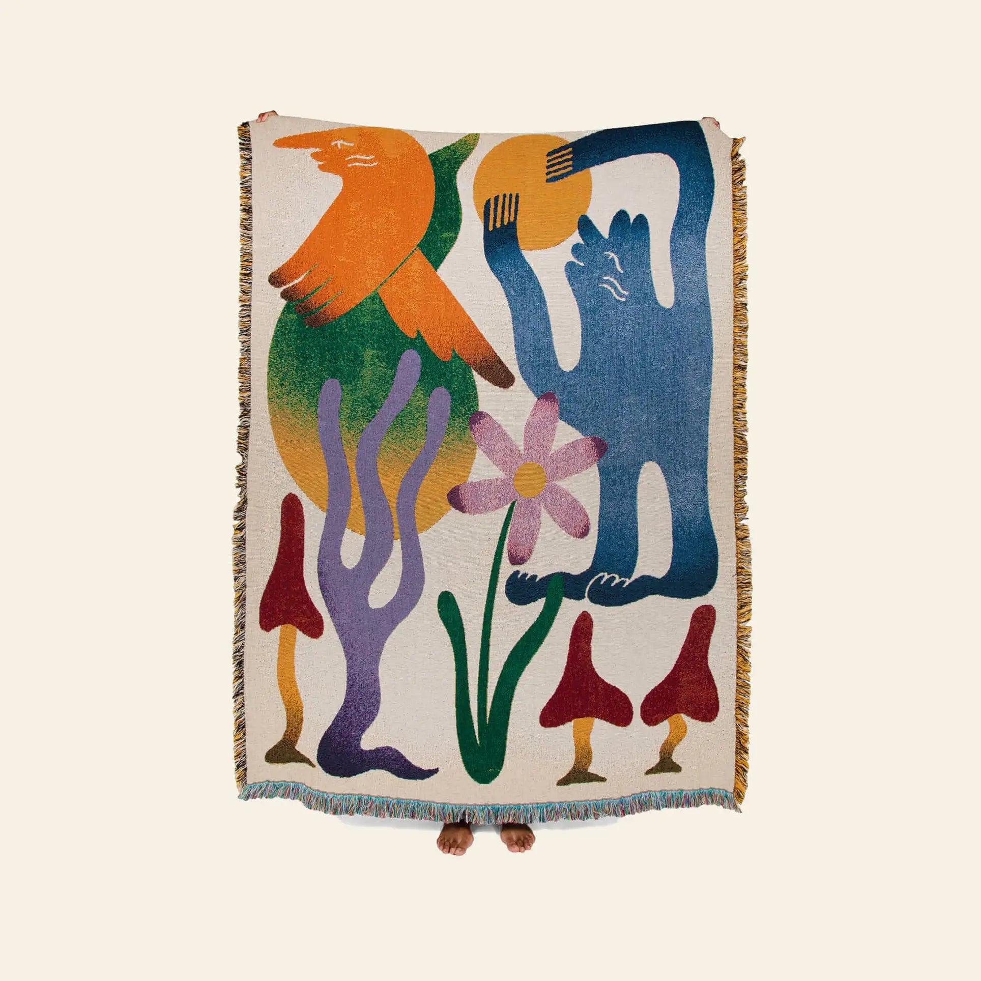The Slowdown Studio Dumont Throw, crafted from recycled cotton by Slowdown Studio, features colorful abstract shapes—a bird, blue figure, flower, mushrooms—and two feet peeking out against a plain backdrop.
