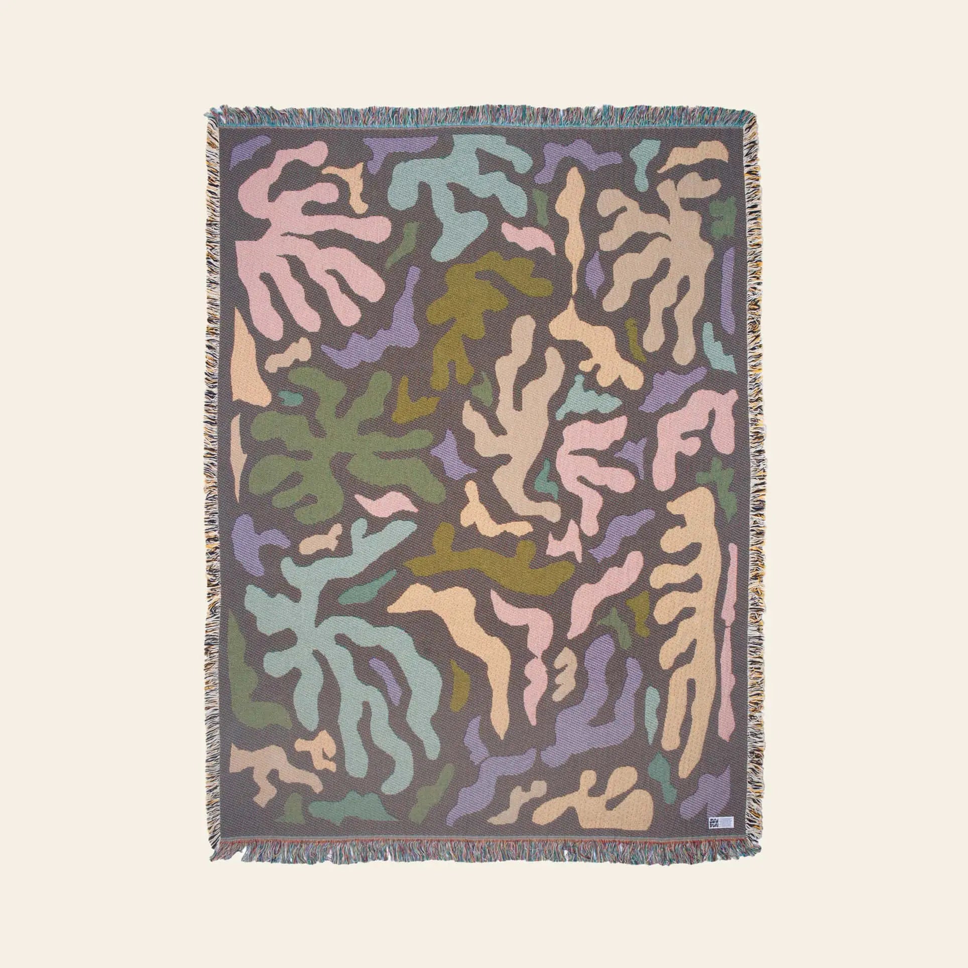 The Slowdown Studio Mercer Throw features a colorful abstract pattern in green, purple, blue, pink, and beige with a fringed border—crafted from recycled cotton for sustainable style.