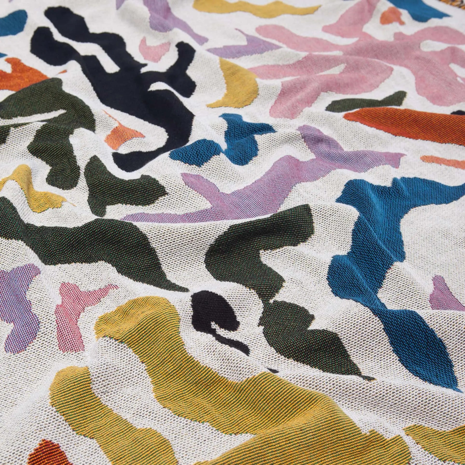 A close-up of the Slowdown Studio Mercer Throw by Slowdown Studio, made from recycled cotton, highlights abstract shapes in black, pink, yellow, green, blue, and coral on a light beige or white background.