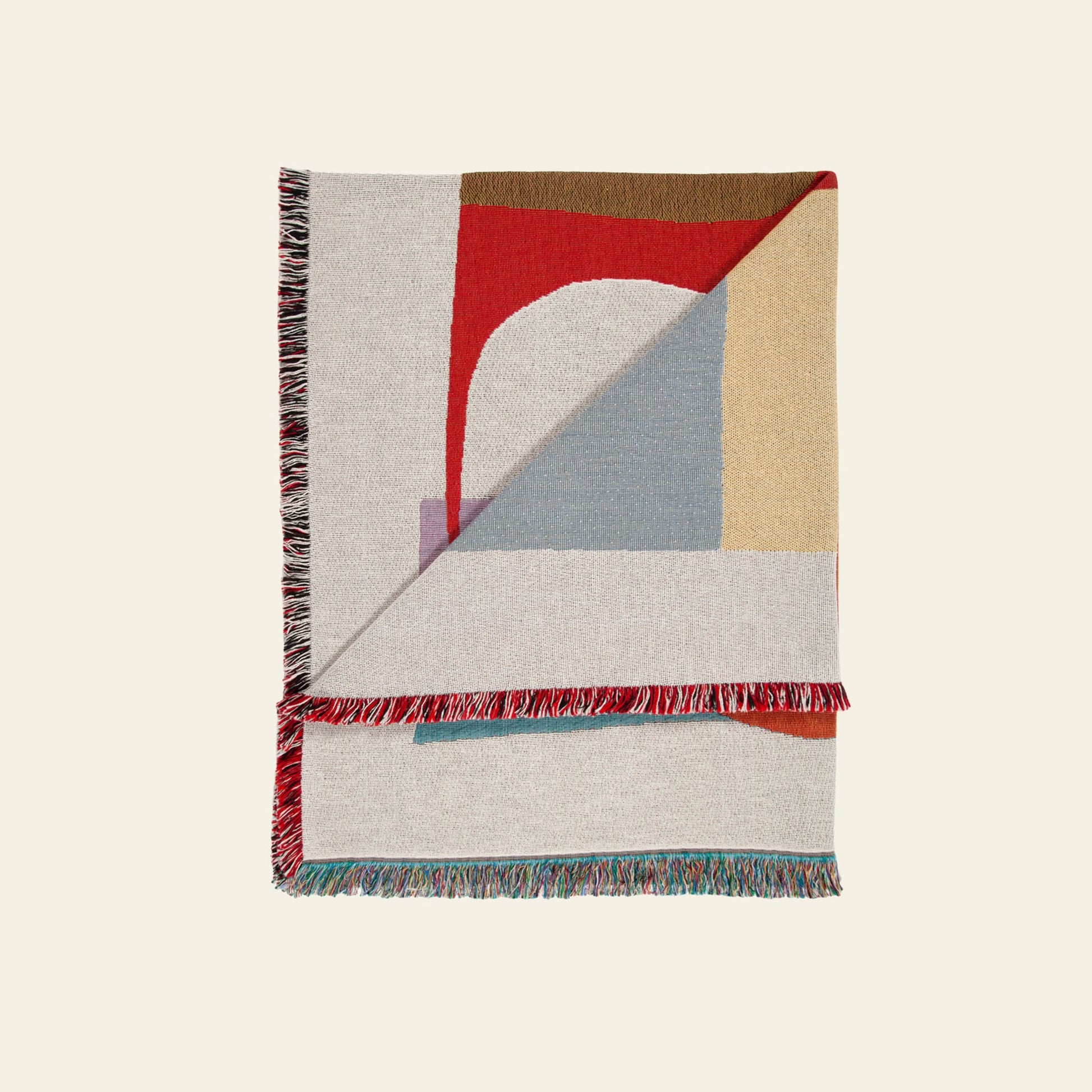 The Slowdown Studio Oroza Throw is a recycled cotton blanket by Slowdown Studio, showcasing abstract geometric patterns in red, beige, grey, blue, and brown with multicolored fringes, folded to display both eco-friendly sides.