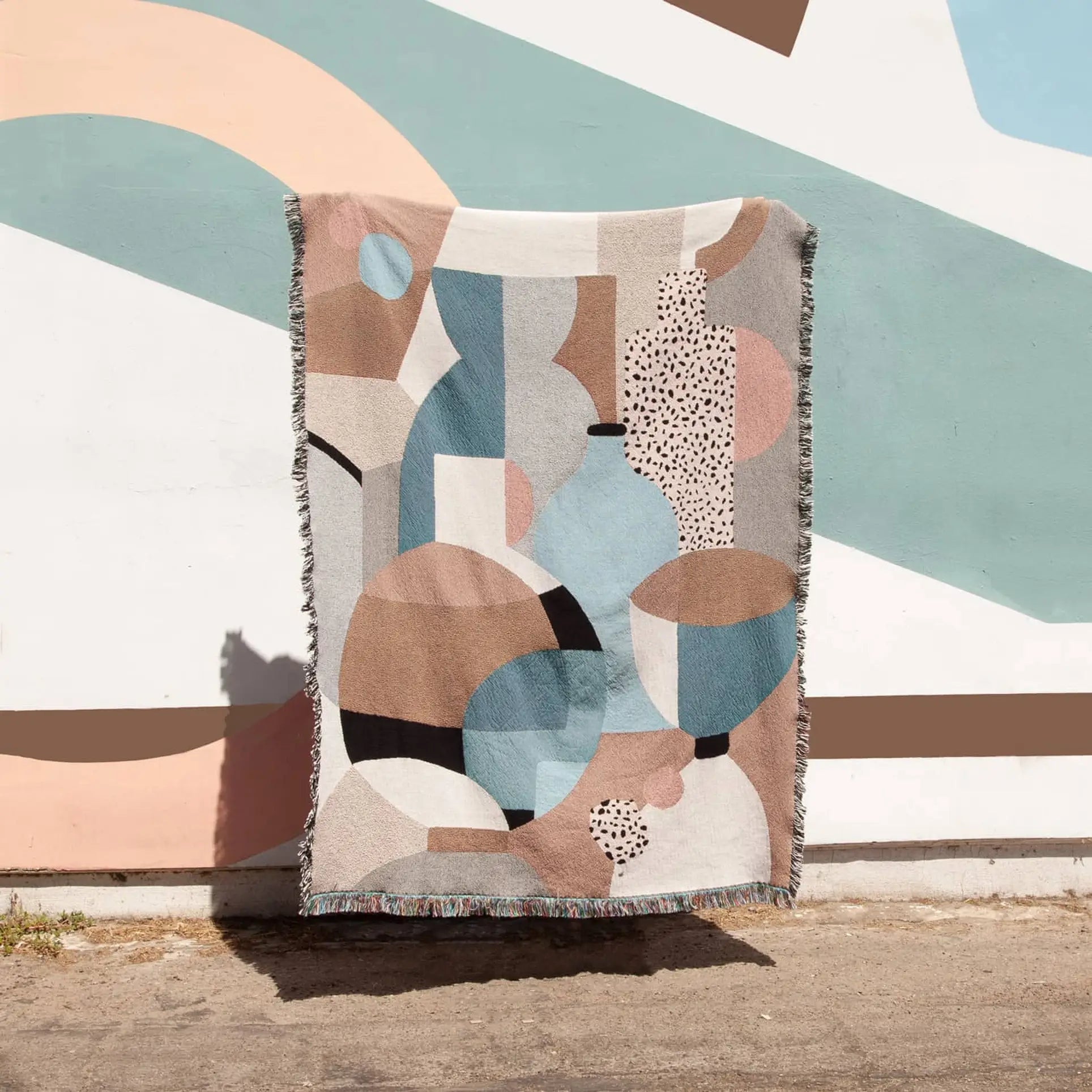 The Slowdown Studio Pollard Throw, made from recycled cotton, showcases an abstract geometric pattern in brown, blue, beige, and black with fringed edges for added texture—a sustainable piece from Slowdown Studio.