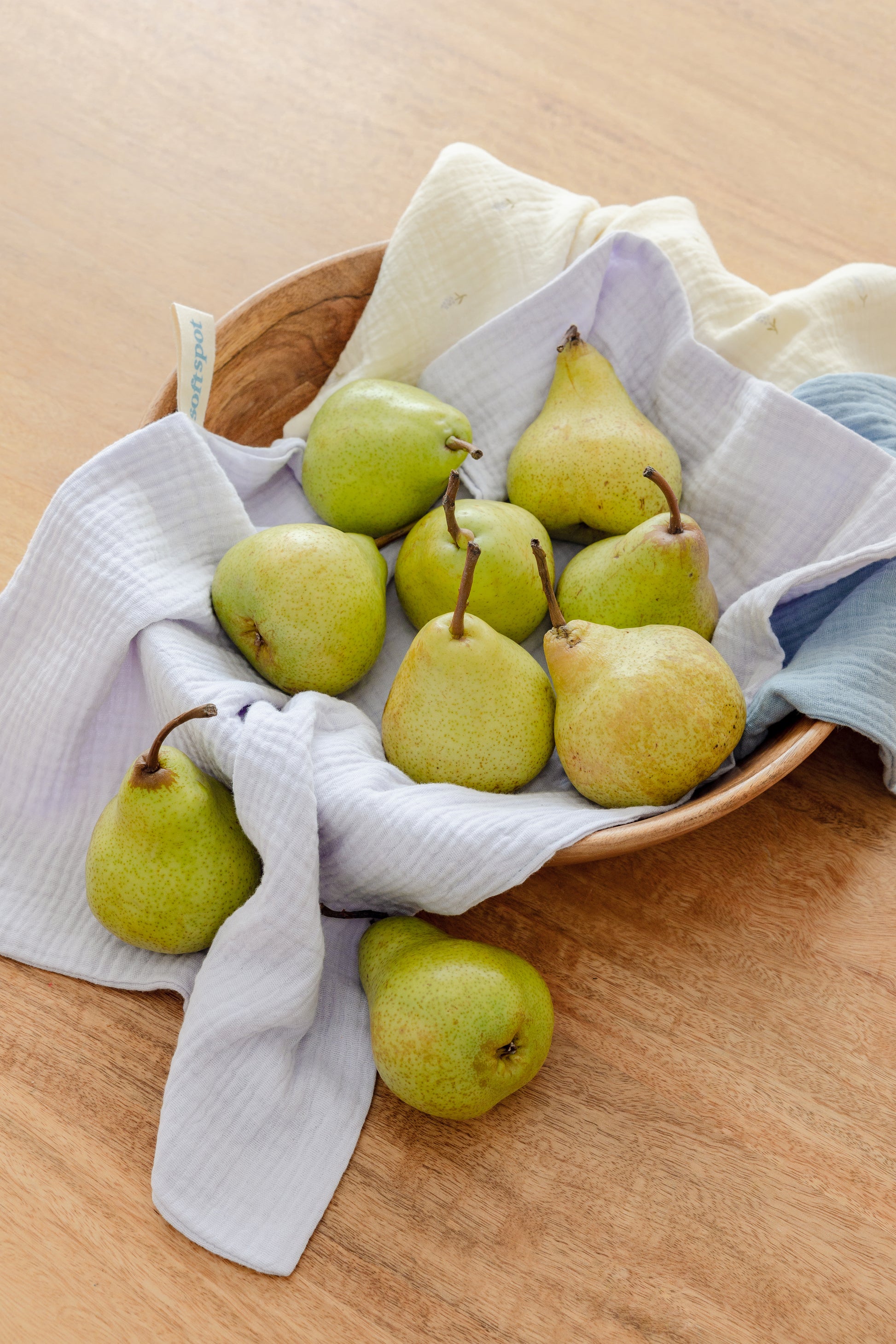 The Soft Spot Soft Tea Towels (Set of 3) by Soft Spot, in cream, blue, and white, hang by labeled loops from a wooden rack against a light gray wall—ideal for use as hand or tea towels.
