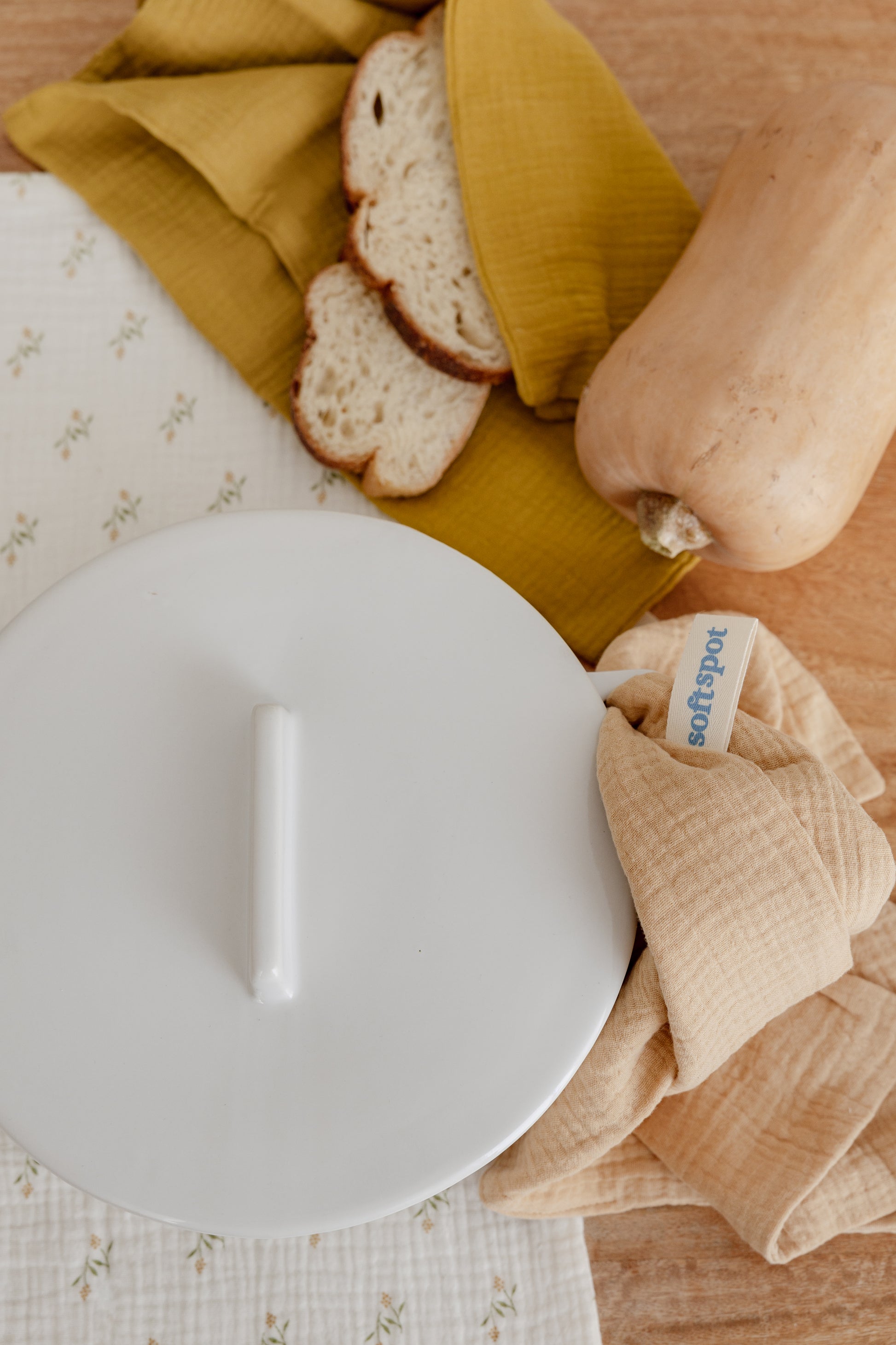 The Soft Spot Soft Tea Towels (Set of 3) by Soft Spot—mustard yellow, white, and brown with a white tag—are neatly folded on a woven rattan chair, perfect as hand towels, placemats, or tea towels.