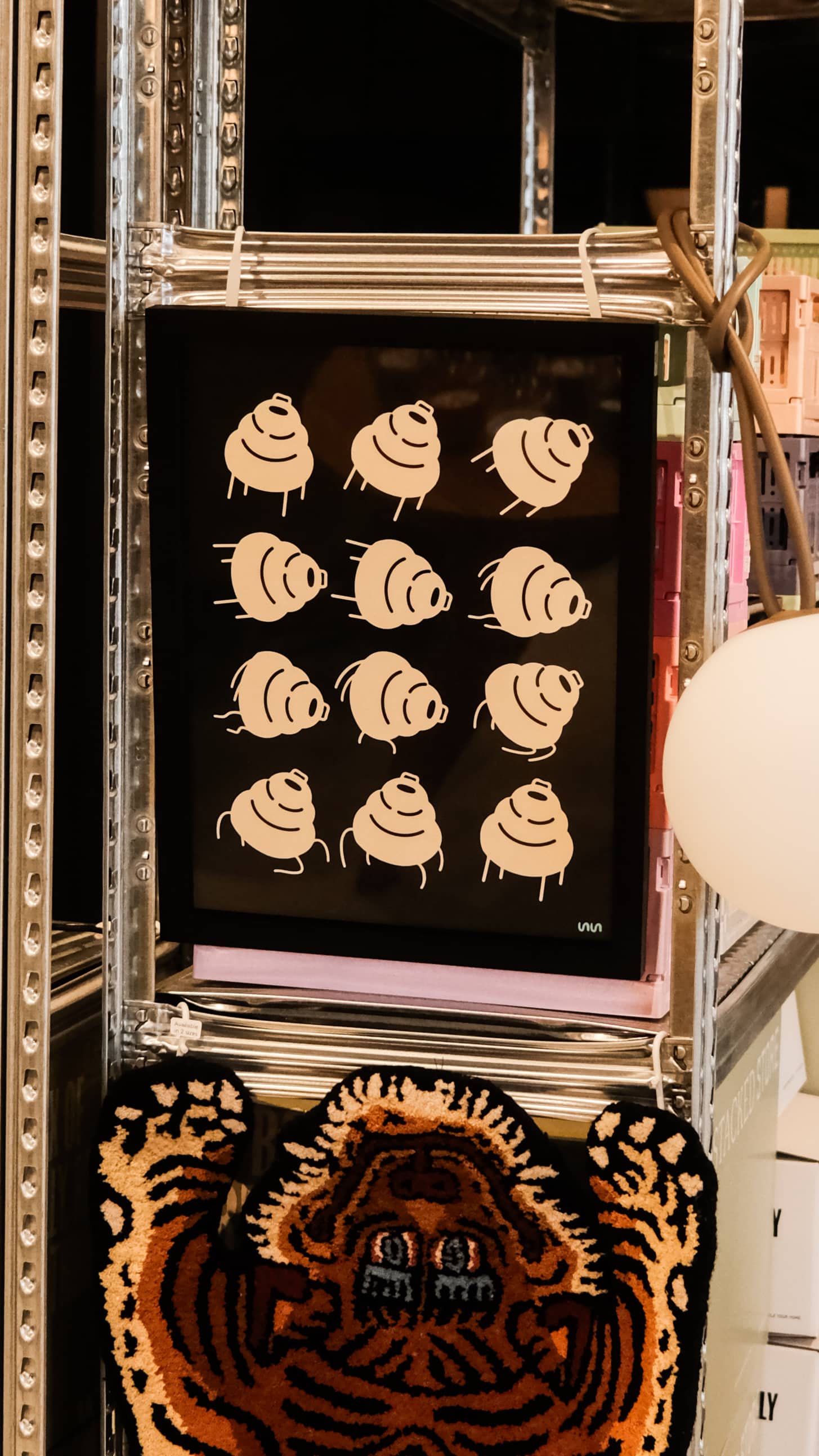 The Stacked Store Trip Poster by Stacked Store is displayed on a metal shelf, complemented by a decorative tiger rug and the minimalist Akari 24N lamp nearby.