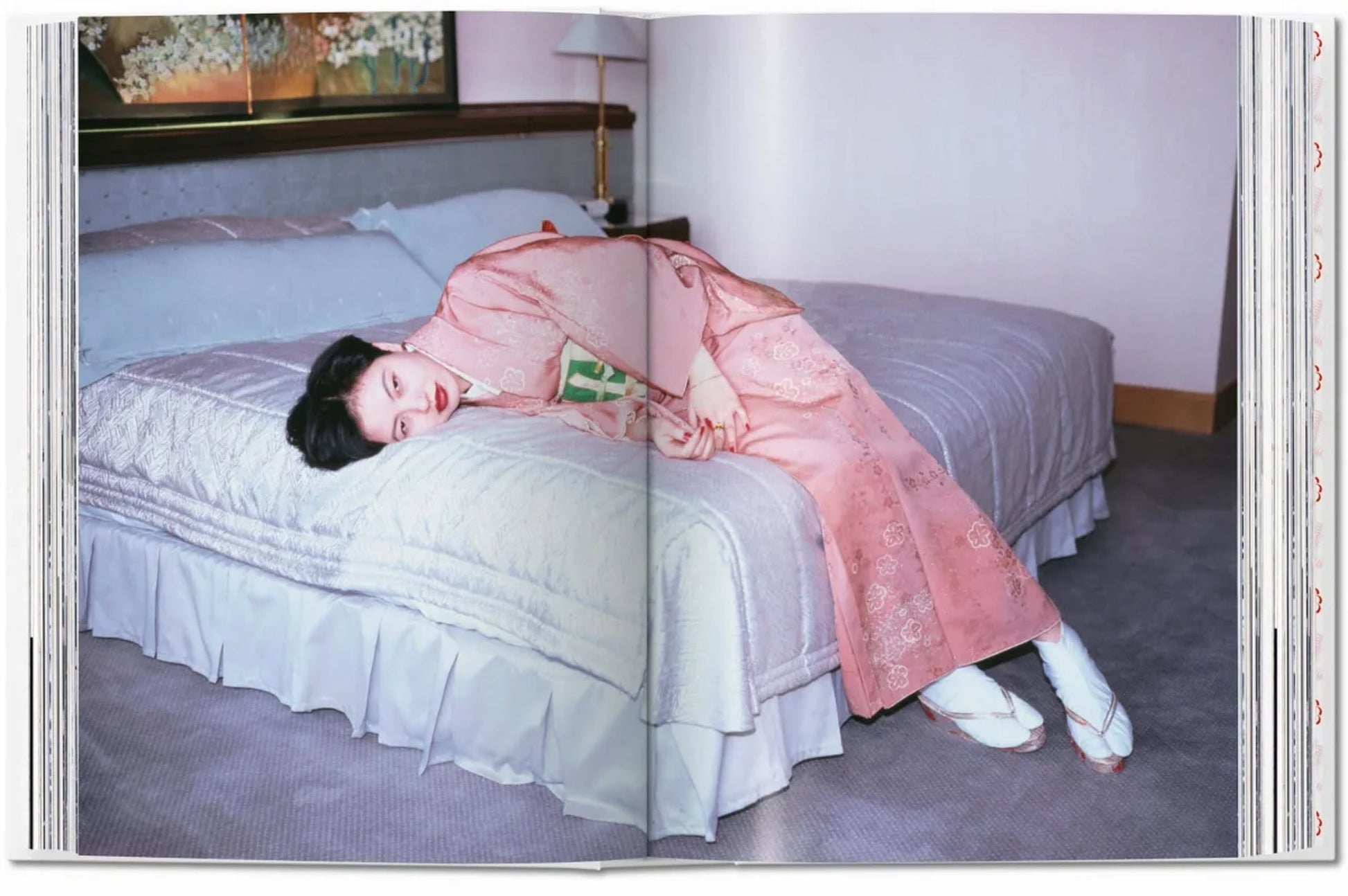 A person in a pink kimono and white slippers lies sideways on a bed in soft light, capturing the intimate style of Nobuyoshi Araki as seen in TASCHENs Araki (40th Edition) from TASCHEN.