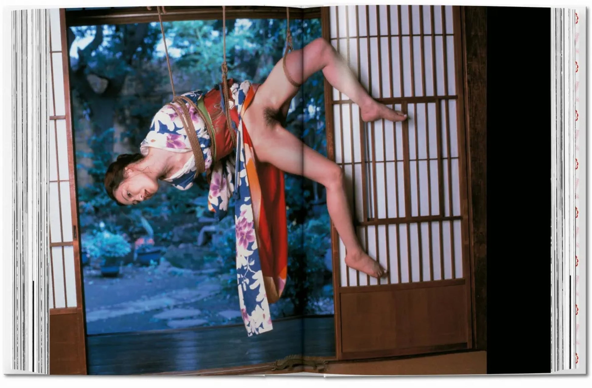 A person in a floral kimono is bound by ropes in a Japanese room with shoji screens, reflecting the style of Nobuyoshi Araki as seen in TASCHENs Araki (40th Edition), with a tranquil garden outside.