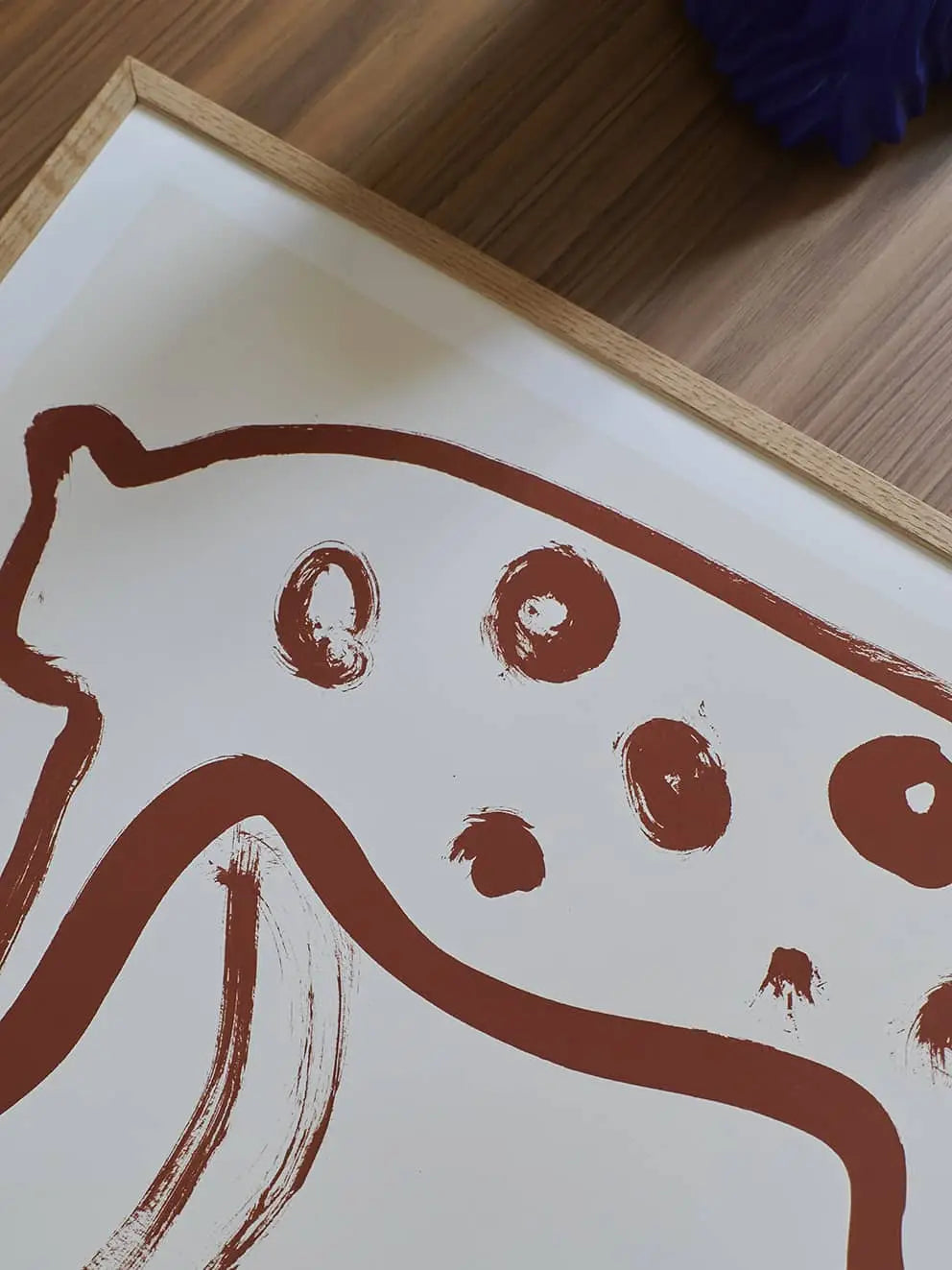 The Poster Clubs Jaguar 01 (50x70) by Anastasia Krasilnikova is a framed minimalist print featuring brown brushstroke art of an abstract jaguar on white, displayed on a wooden surface. Available at The Poster Club.