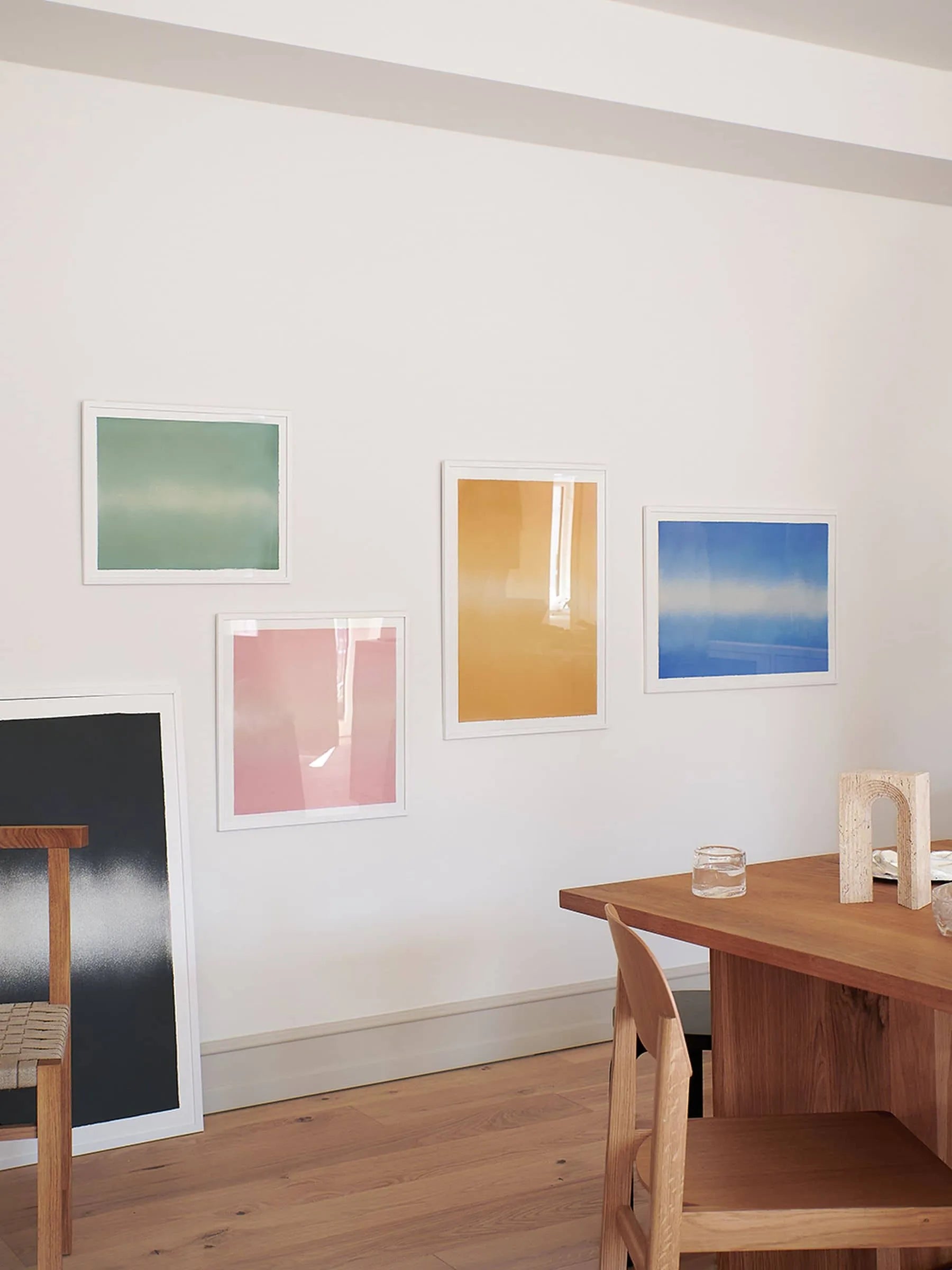 A minimal dining space with a wooden table, chairs, clear glasses, and Anne Nowak - Yellow Interstellar (30x40) by The Poster Club hanging on a white wall.