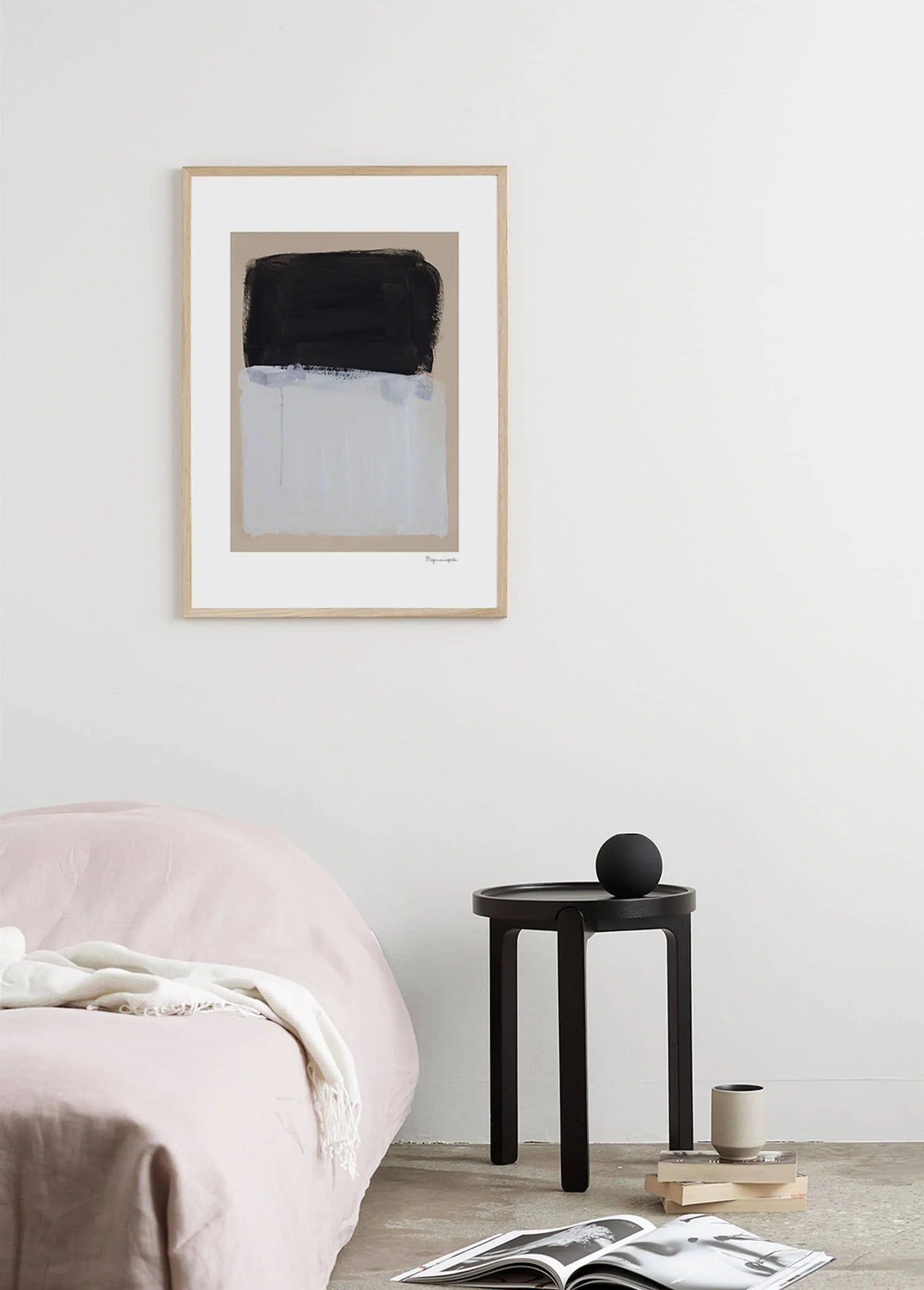 Minimalist bedroom with a light pink bed, small black side table holding a round object and cup, and Berit Mogensen Lopez - Painted Surface (30x40) art print by The Poster Club featuring black, white, and beige shapes on the white wall.