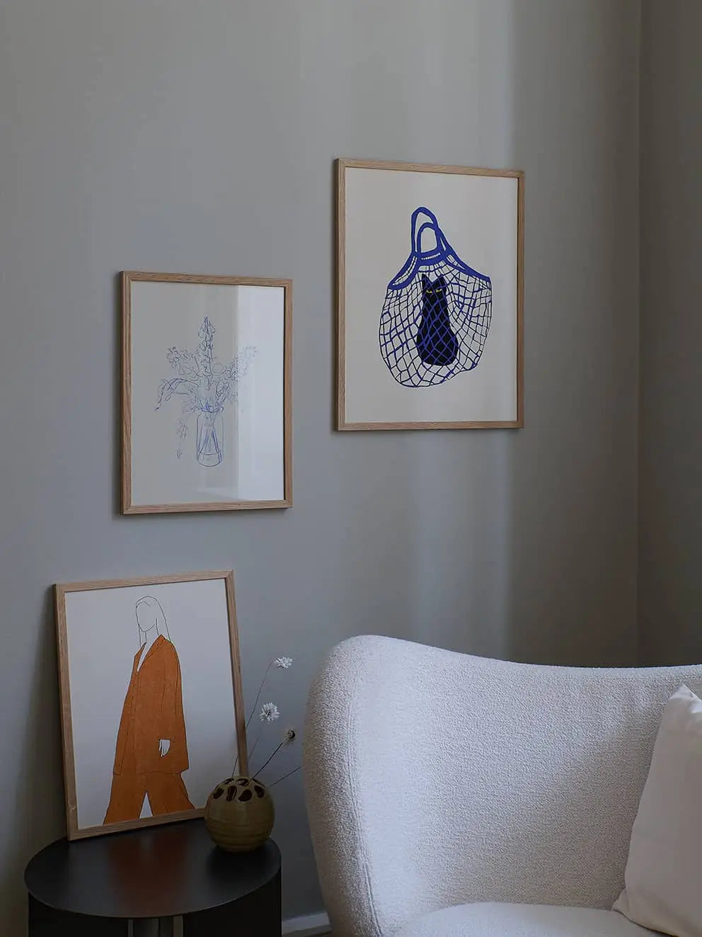 A cozy corner with a white textured armchair, a black side table, and Monday (30x40) by Anna Johansson from The Poster Clubโa chic art print displayed on the gray wall.