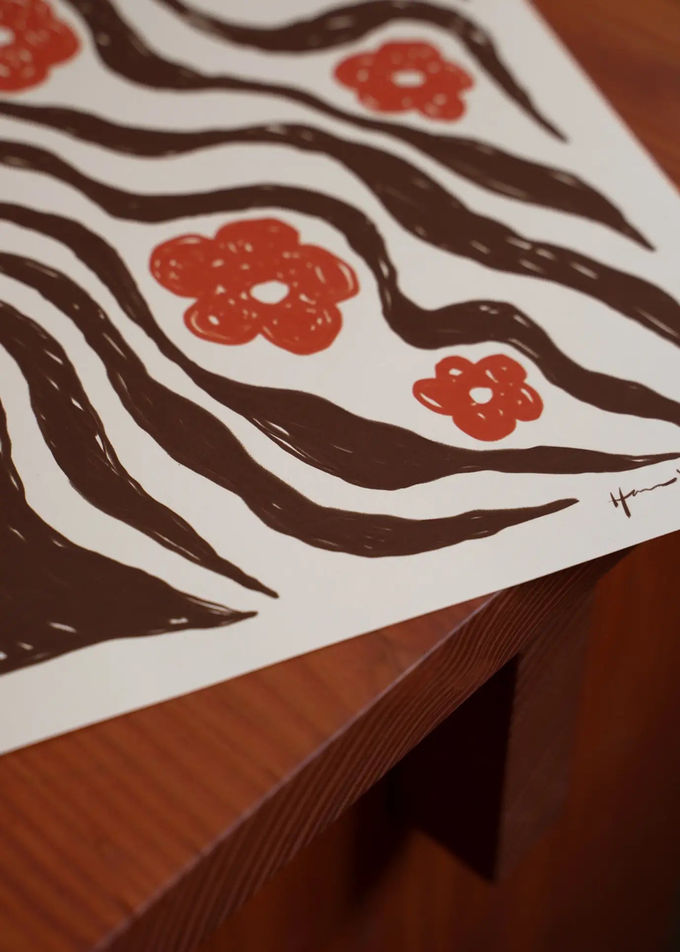 A close-up of The Poster Club Hanna KL - Flux (30x40) art print, showing wavy black lines and red flowers on white paper atop a wooden surface. From The Poster Club collection.