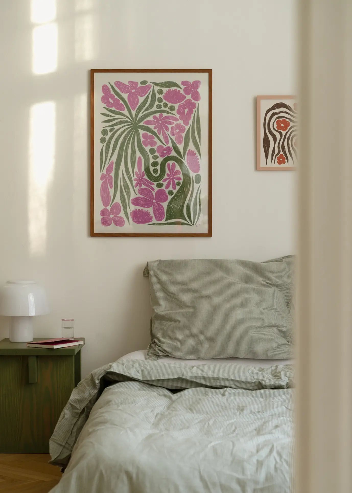 A cozy bedroom with a neatly made bed in light gray bedding, a green nightstand, and The Poster Clubs Hanna KL - Wonder (50x70) art print displayed above the bed amid colorful floral and abstract designs on the white wall.