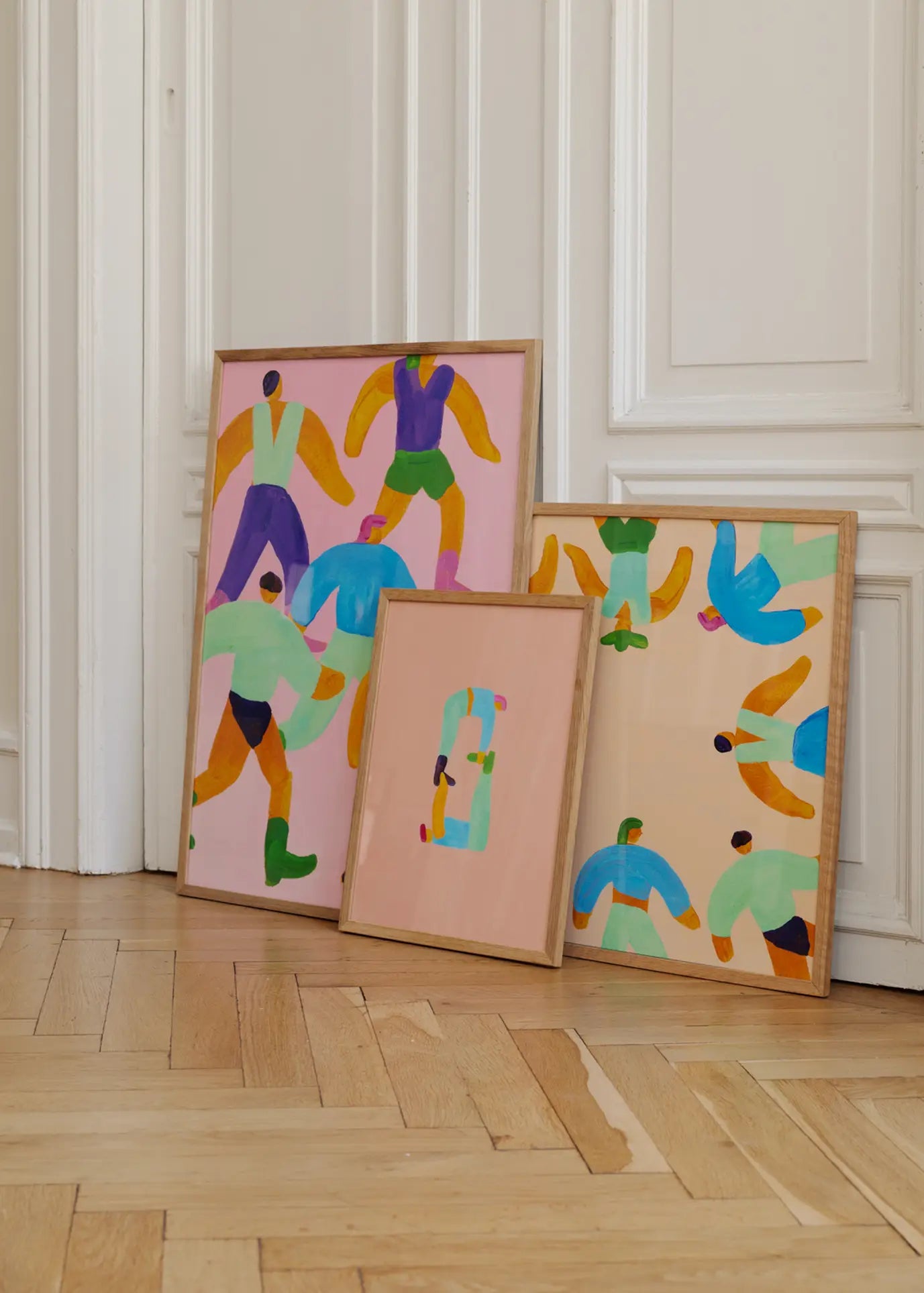 The Poster Club Lise Uhrskov - Walk The Walk (50x70) fine art print features bold, stylized human figures in vibrant colors on pastel backgrounds, displayed in a wooden frame against a white paneled wall and wooden floor.