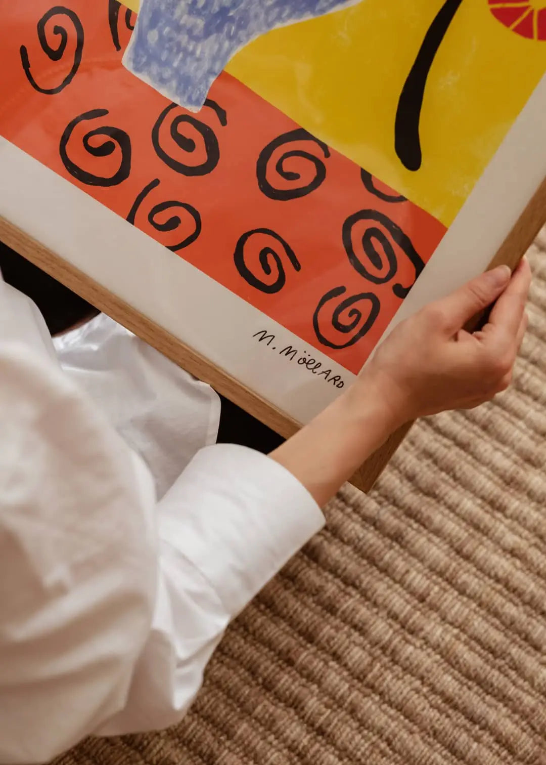 A person in a white shirt holds Flowers in Blue Vase (50x70) by Madelen Möllard, a colorful art print from The Poster Club featuring red, yellow, and blue shapes with black spirals and the artist’s signature visible.