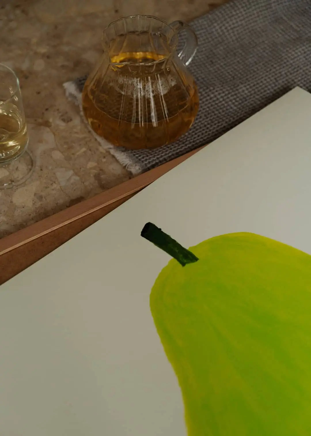 A glass and a carafe of a light drink rest on a table beside The Poster Club Berit Mogensen Lopez - Bloom (50x70) art print, creating a serene scene that reflects The Poster Club’s curated elegance.
