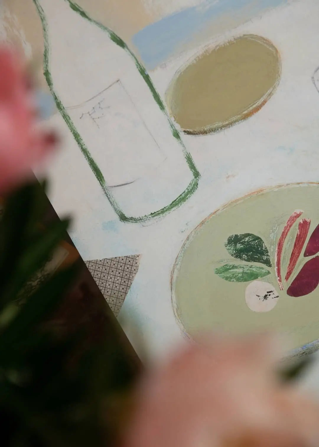 The Poster Club’s Bloom (50x70) by Berit Mogensen Lopez features soft-focus pink flowers that partially obscure a green bottle, abstract vegetables on a plate, and an oval object set against a pale background.