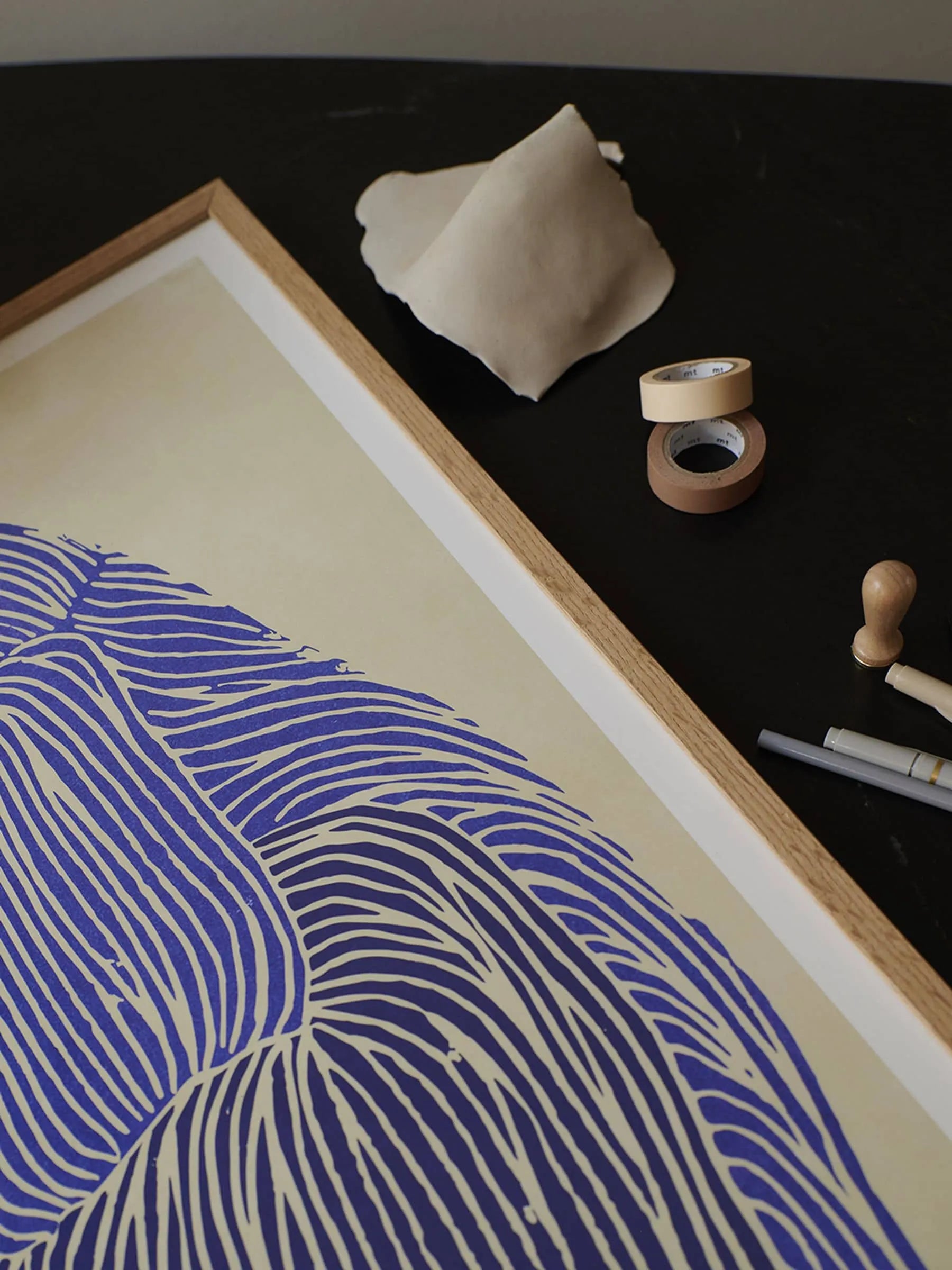 Rebecca Hein - Deep Blue (30x40) from The Poster Club showcases blue curved lines on beige, displayed with masking tape, off-white fabric, a pen, and a stamp—evoking Rebecca Hein’s ocean-inspired style.