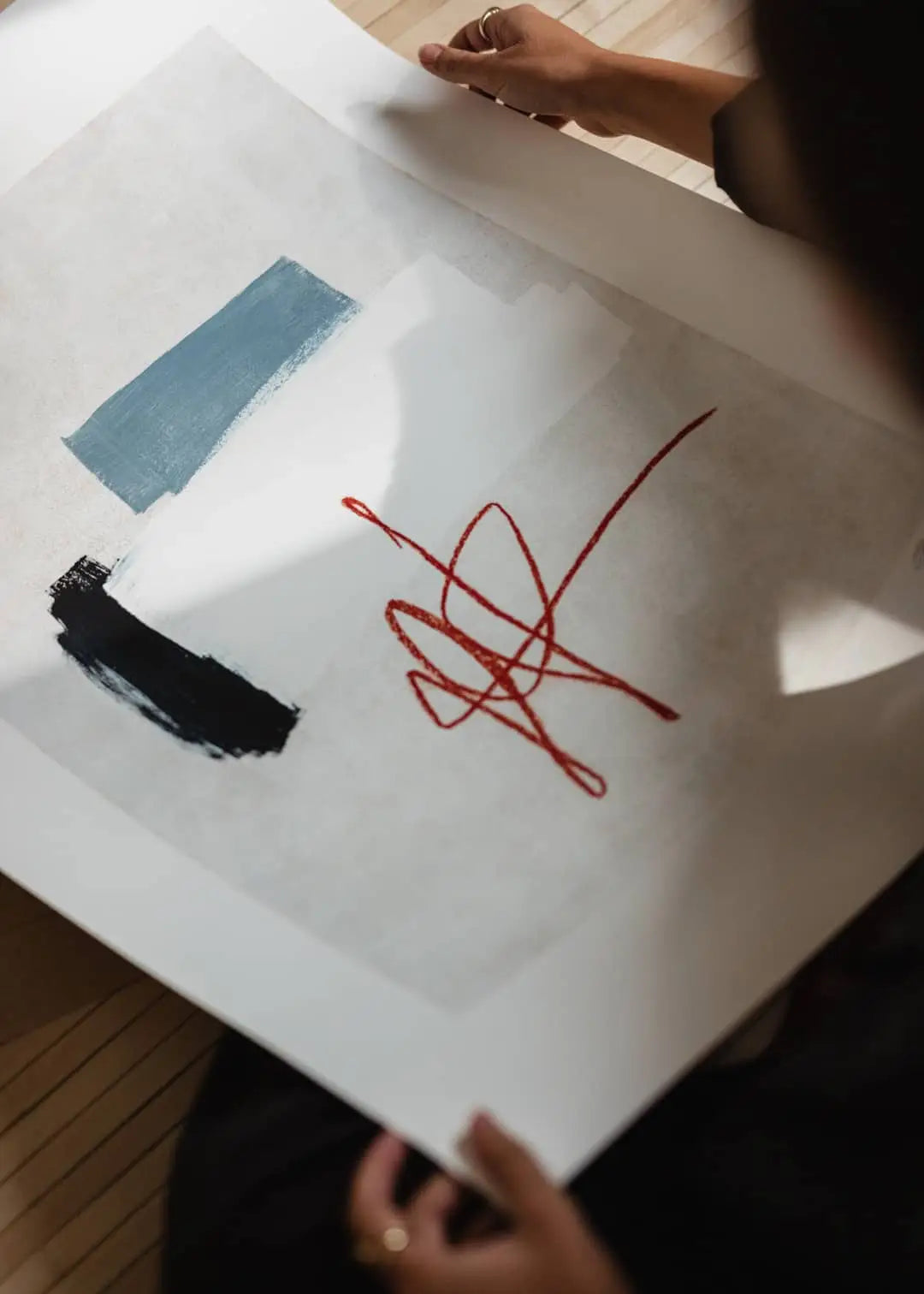 A person holds Flowers in Blue Vase by Madelen Möllard for The Poster Club (50x70), an abstract art print with black and blue forms, a white area, and red details on a light background, partially shadowed.