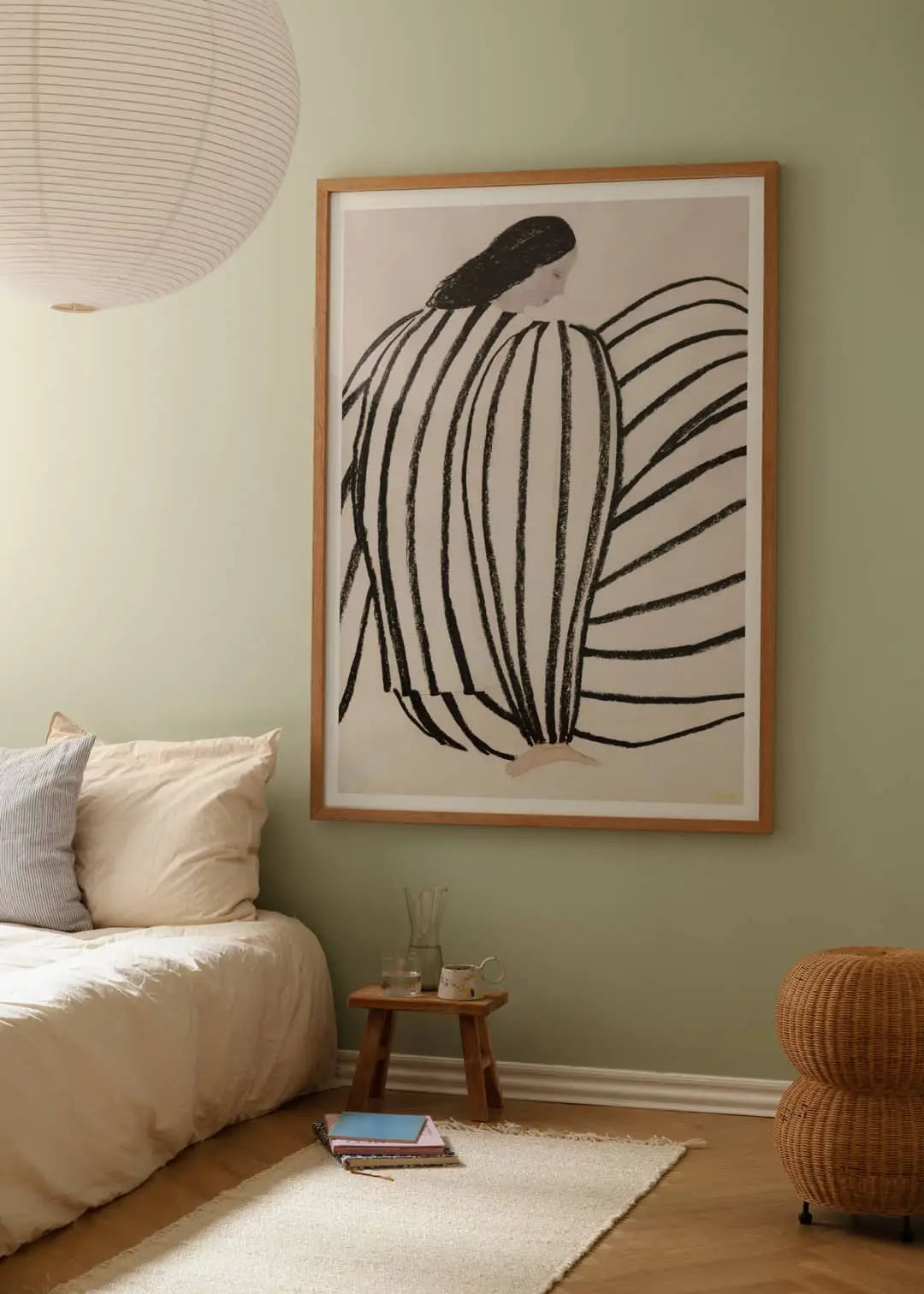A cozy bedroom with light green walls, a low bed with cream bedding, a woven ottoman, and The Poster Club Berit Mogensen Lopez – Improvise (50x70) art print featuring abstract black lines.