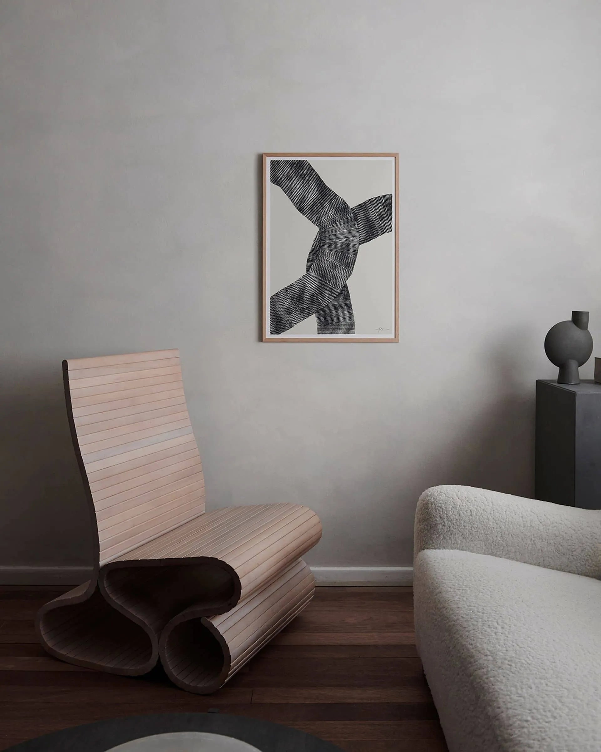 A modern minimalist room with Scandinavian design, featuring a curved wooden chair, textured white armchair, round table, black cabinet, and The Poster Club’s Studio Paradissi - Abstract 697 (30x40) art print on a light gray wall.