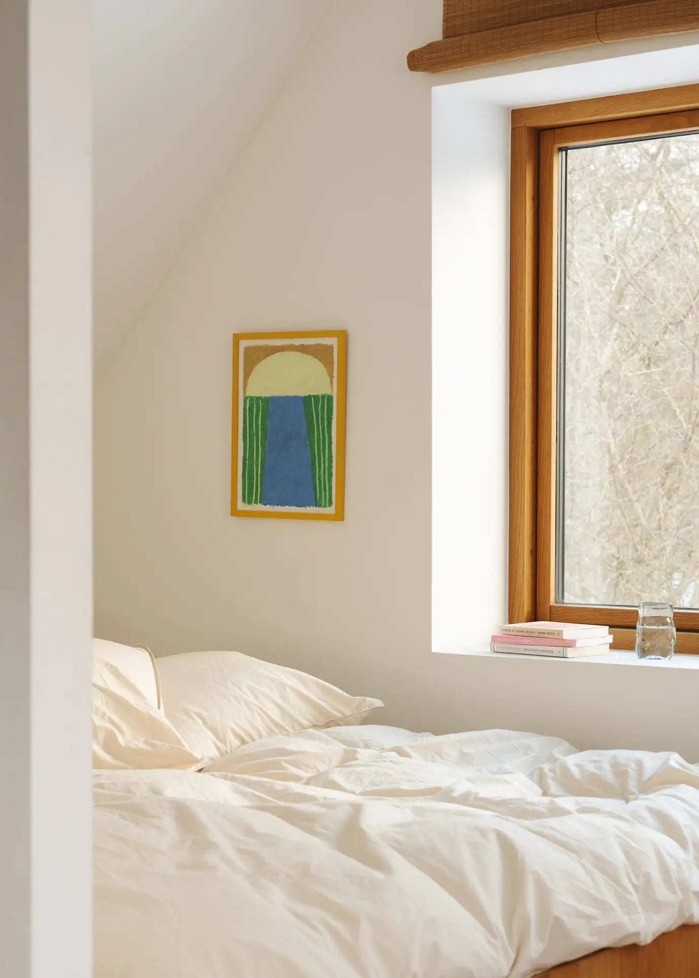 A bright, minimalist bedroom features a neatly made bed with cream bedding, sunlight streaming through a wooden-framed window, and The Poster Club’s Suzanne Lustig - Laughing Jim (30x40) art print adding character to the crisp white wall.