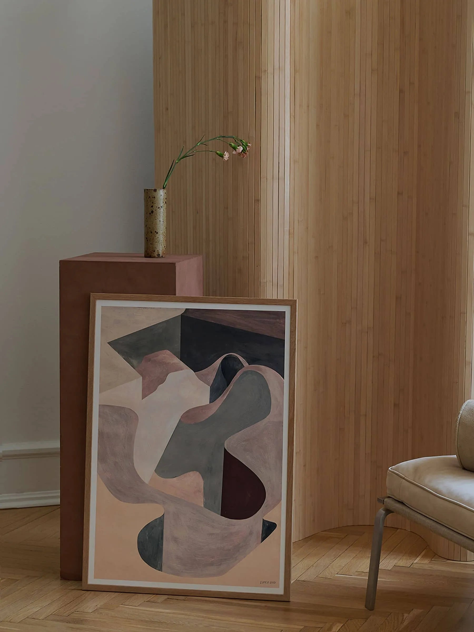 The Poster Club’s The Lipko Project - Empty Skatepark 02 (30x40) fine art giclée print in muted tones leans against a brown pedestal with a tall vase and single flower, accented by light wood paneling and a beige chair for a minimalist look.