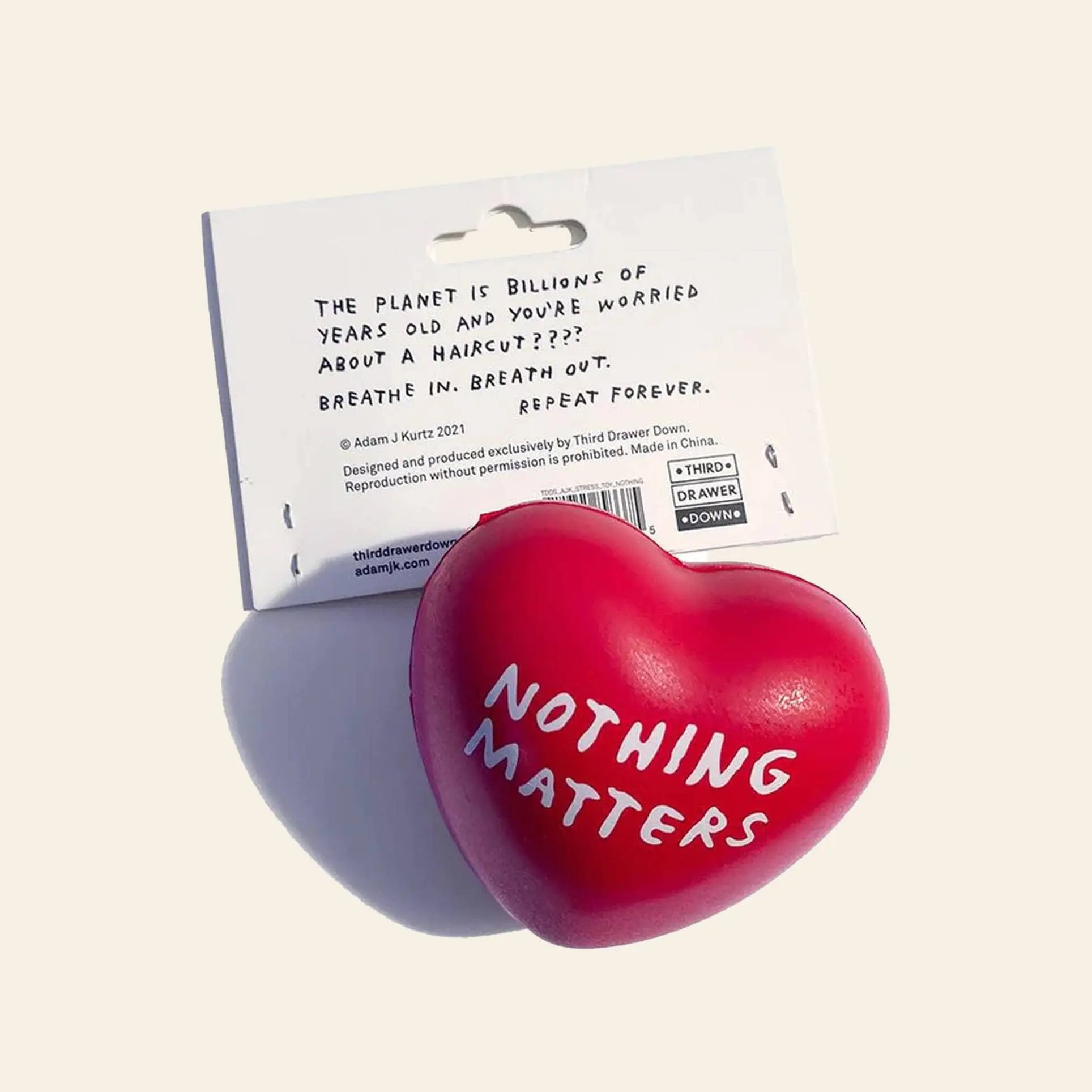 The Third Drawer Down Adam JK - Nothing Matters Stress Toy is a red heart-shaped squishy with “NOTHING MATTERS” in white, shown in front of a card reading: The planet is billions of years old and you’re worried about a haircut??? Breathe in. Out. Repeat.
