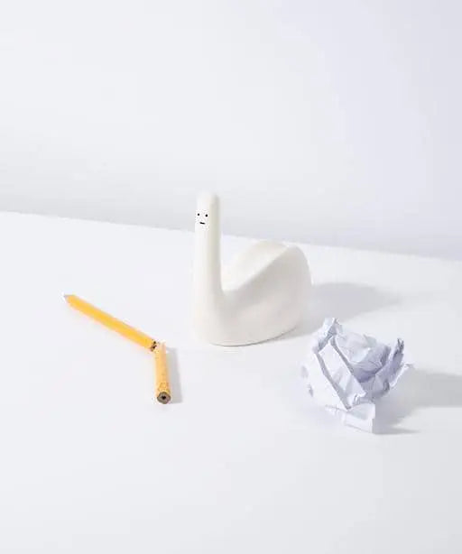 A broken yellow pencil, a crumpled piece of white paper, and the Third Drawer Down David Shrigley - Ridiculous Stress Swan-Thing are arranged on a white surface against a plain white background.
