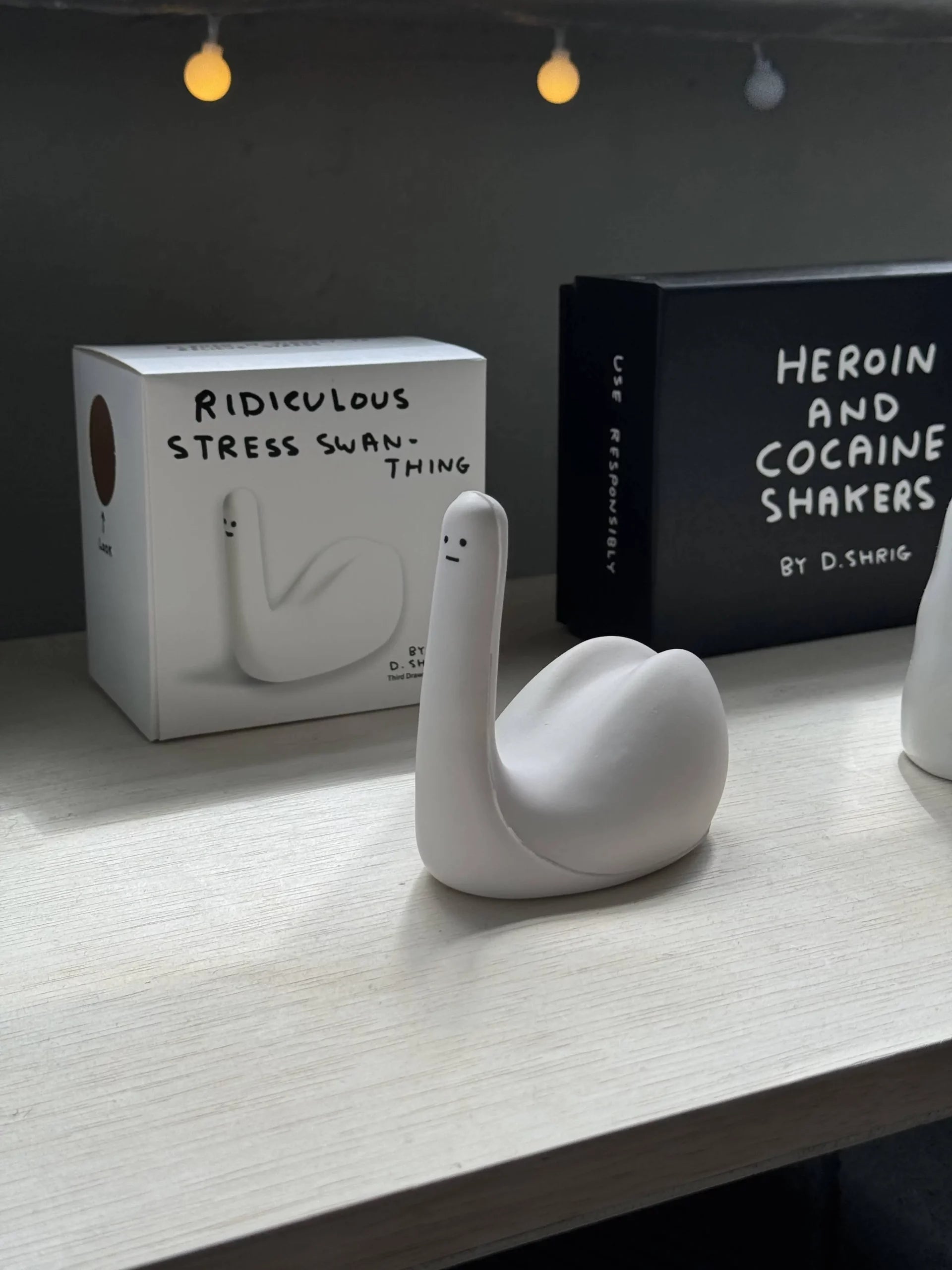 The Third Drawer Down David Shrigley - Ridiculous Stress Swan-Thing, a quirky white ceramic swan figurine by Third Drawer Down, sits beside its box and a book—perfect as a fun, stress-free gift for any shelf.