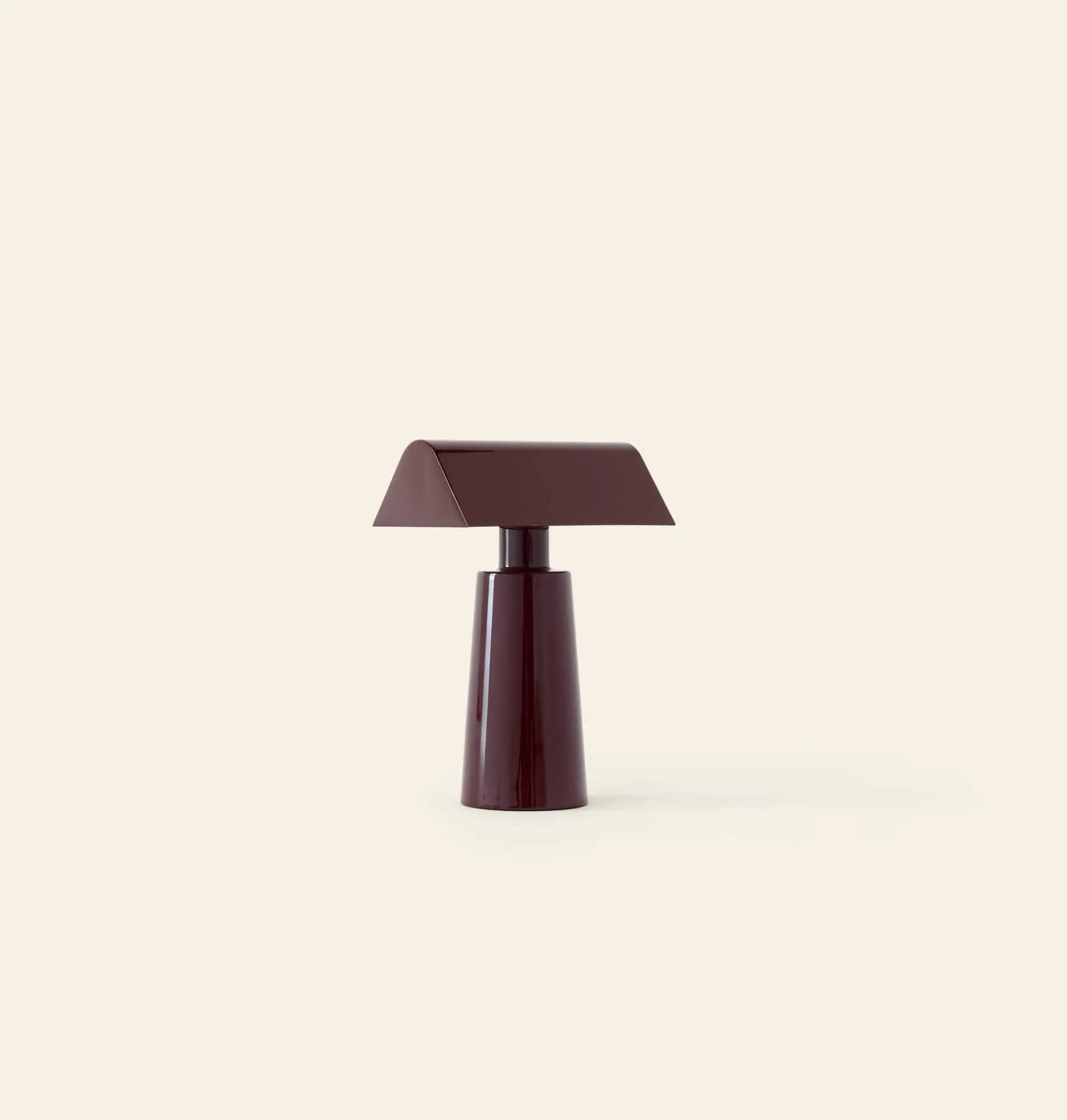 The &Tradition Caret MF1 Portable Table Lamp by &Tradition features a modern, minimalist design with a dark burgundy finish, a rectangular slanted shade, and conical base, set against a plain beige background.