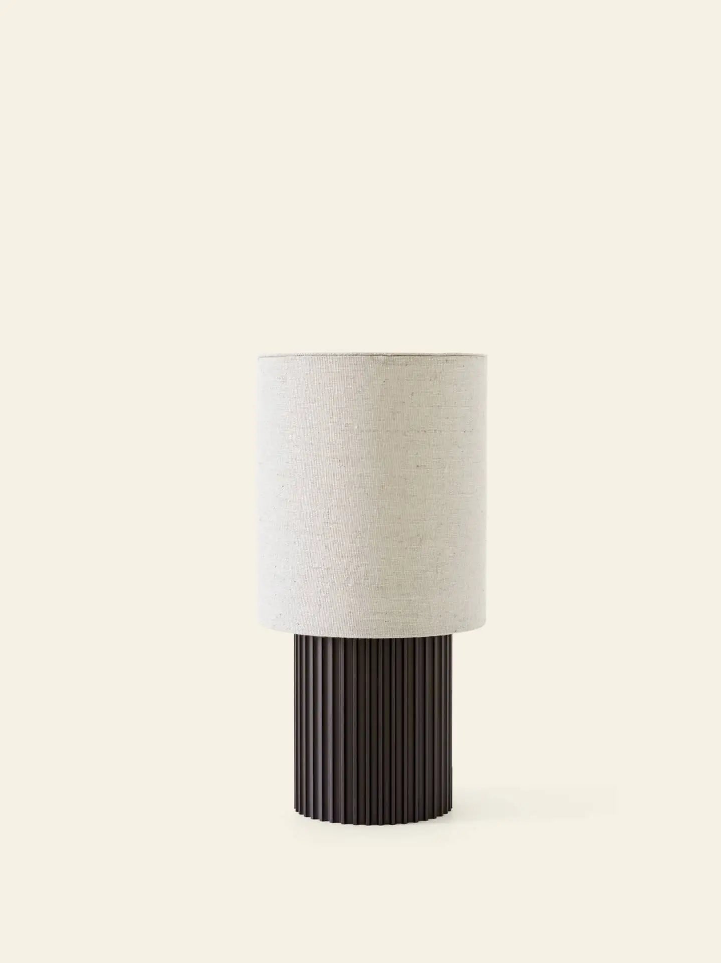 The &Tradition Manhattan SC52 Portable Table Lamp features a cylindrical, ribbed black base and a round off-white fabric shade. Its industrial-inspired design by &Tradition adds modern style to contemporary interiors.