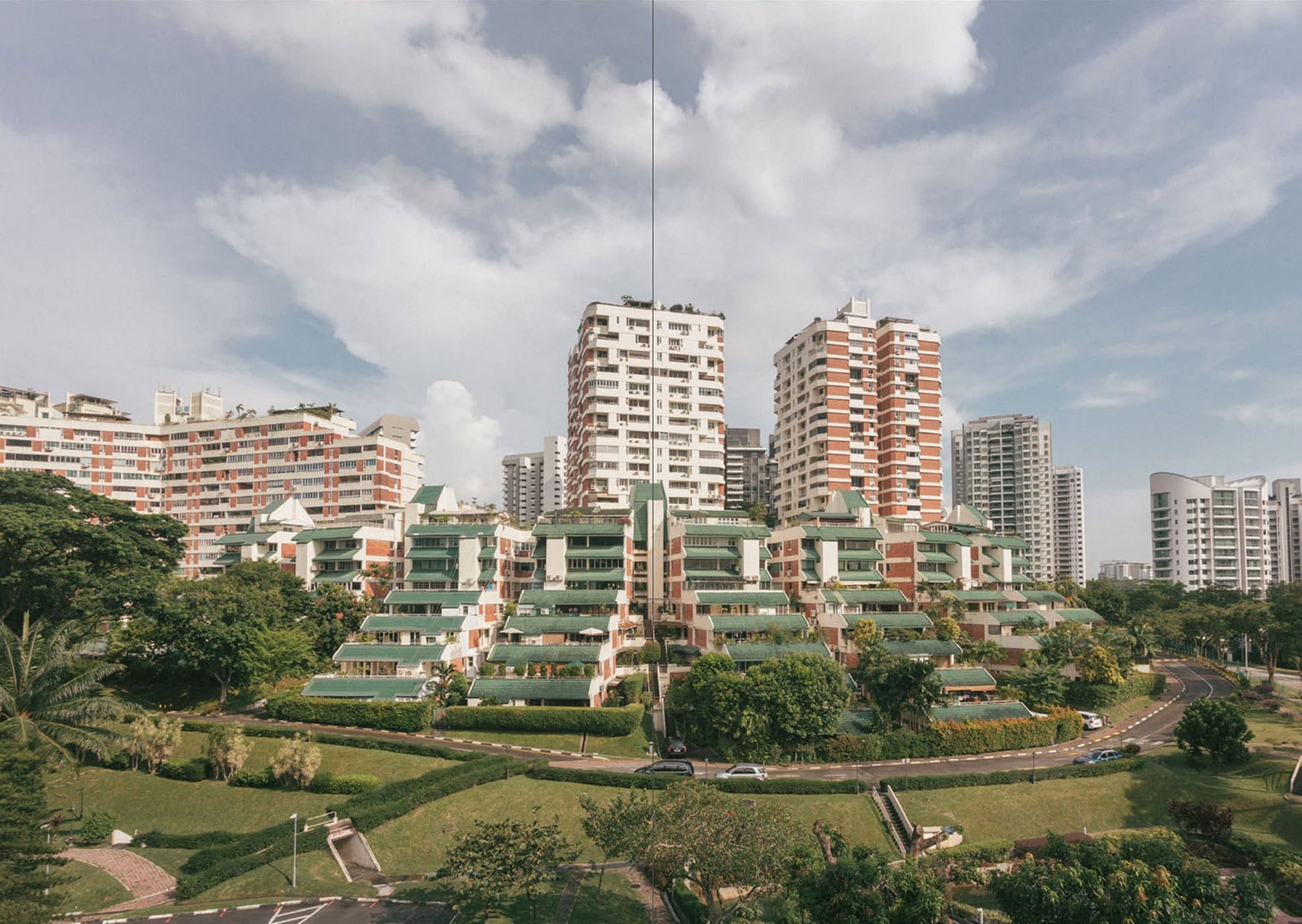 UNIT. A Glimpse Into Singapore’s 1970s - ’80s Private Apartments showcases colorful mid-rise homes set amid greenery and roads, with taller towers in the background beneath a partly cloudy sky.