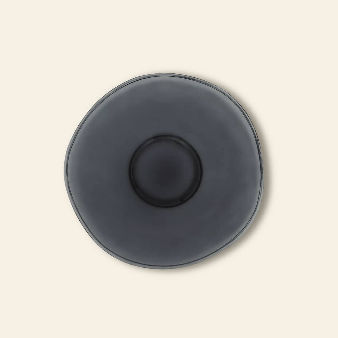 A top view of the Urban Nature Culture Breakfast Plate, crafted from recycled glass with an organic round shape in dark gray, sits on a beige background—ideal for those who cherish sustainable living.