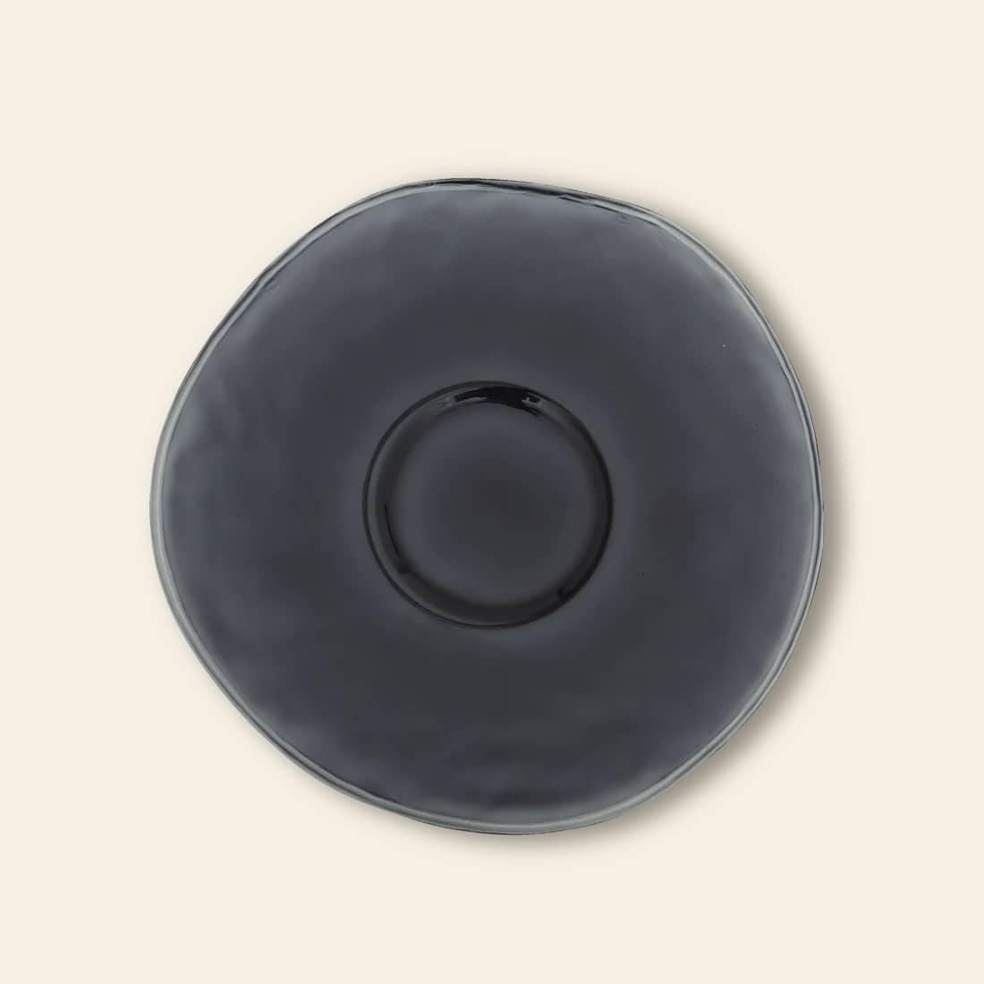 The Urban Nature Culture Dinner Plate Recycled Glass features a round, organic shape with a glossy dark gray finish, adding rustic charm when set against a plain light beige background.
