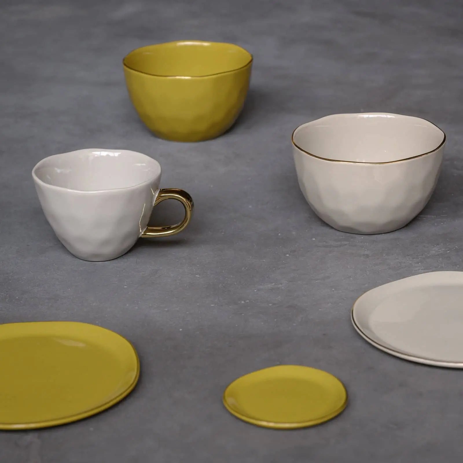 Urban Nature Cultures ceramic collection features pale yellow and off-white cups and plates arranged on gray, plus the Urban Nature Culture Good Morning Bowl in soft pink pastel—ideal for breakfast—and textured cups with gold accents.