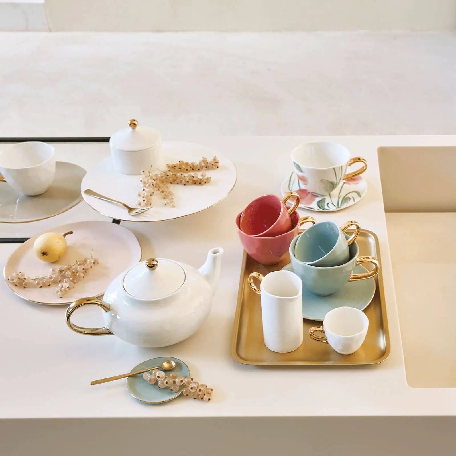 A pastel tea set with white, blue, and pink cups, golden spoons, a teapot, and the Urban Nature Culture Good Morning Breakfast Plate is arranged on a white table with flowers and a gold tray—ideal for Urban Nature Culture style.