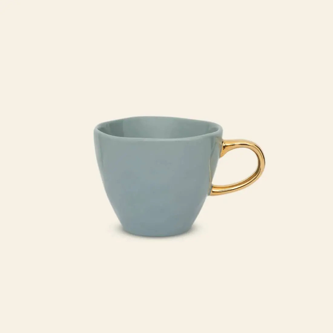 The Urban Nature Culture Good Morning Cup Mini by Urban Nature Culture, a light blue ceramic cup with a shiny gold handle, is centered on a plain beige background.