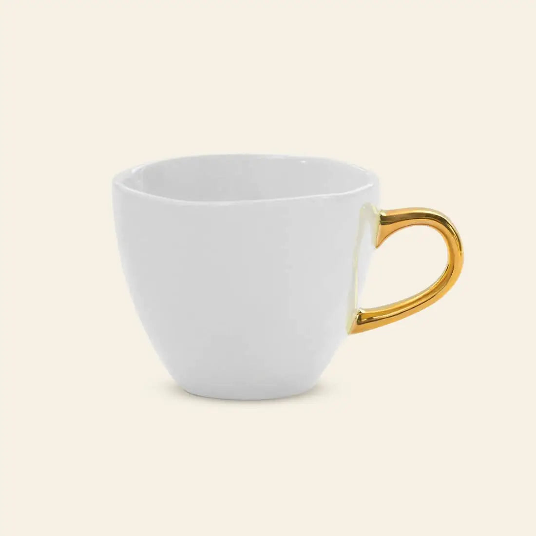 The Urban Nature Culture Good Morning Cup Mini, a plain white ceramic cup with a shiny gold handle by Urban Nature Culture, is shown against a light beige background.